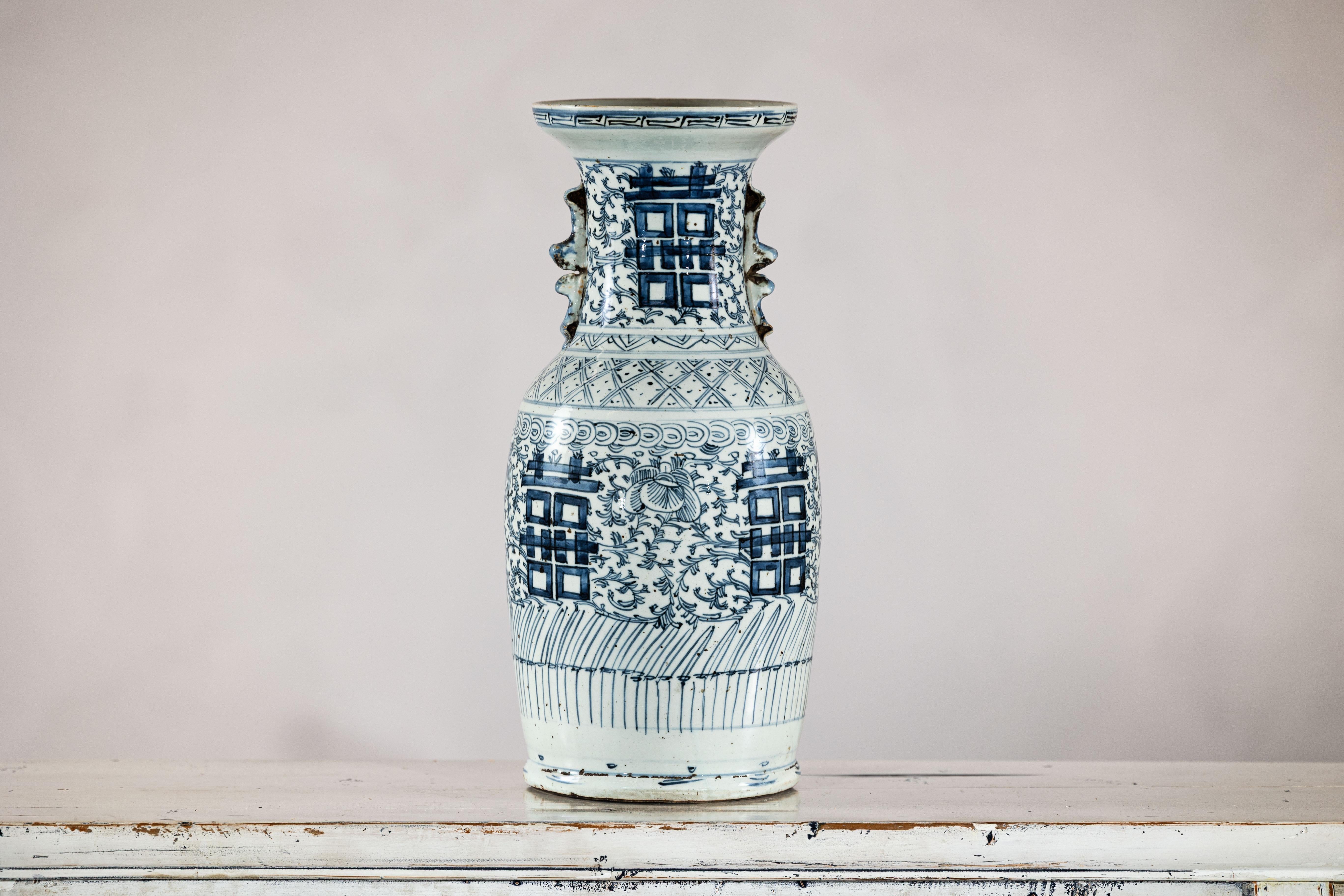 This tall blue and white Chinese altar vase features a boldly hand-painted double happiness motif, surrounded by floral scrolls and geometric patterning in traditional cobalt glaze. Likely dating to the early 20th century, the piece was designed for
