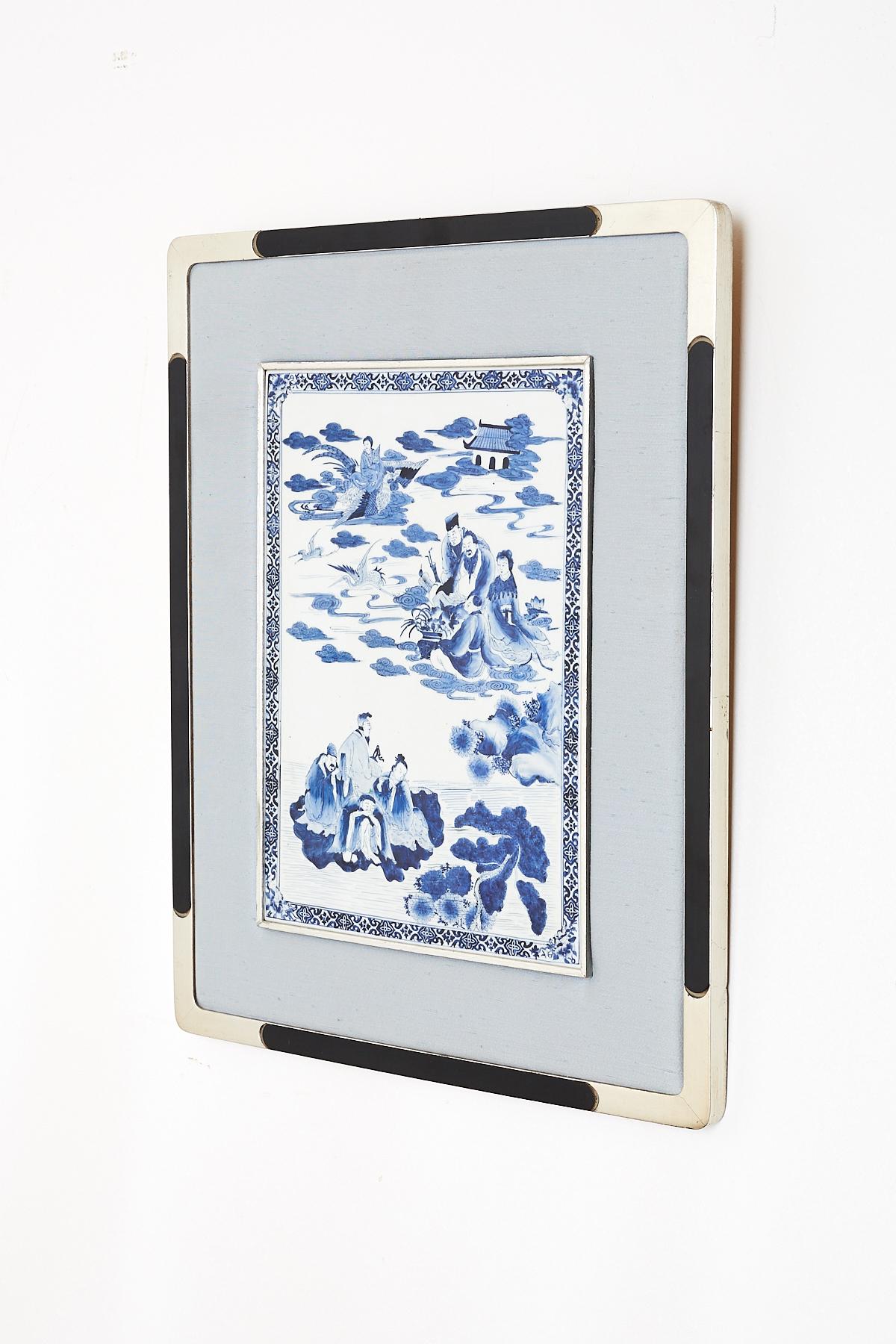 Distinctive Chinese blue and white porcelain plaque depicting deities. Features several figures in clouds with mythical birds and pagodas. Mounted to a silvered frame with a light sky blue silk border. Plaque measures 10.% inches by 14.5 inches.