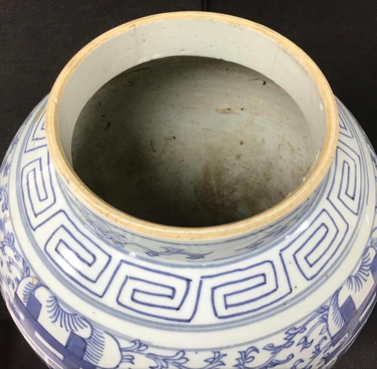 This blue-and-white temple jar stands tall with broad shoulders that taper to a splayed base. Bordered by a simple meander at the neck, the jar is decorated with a dense pattern of orchid blossoms and trailing vines. On each side of the jar, the