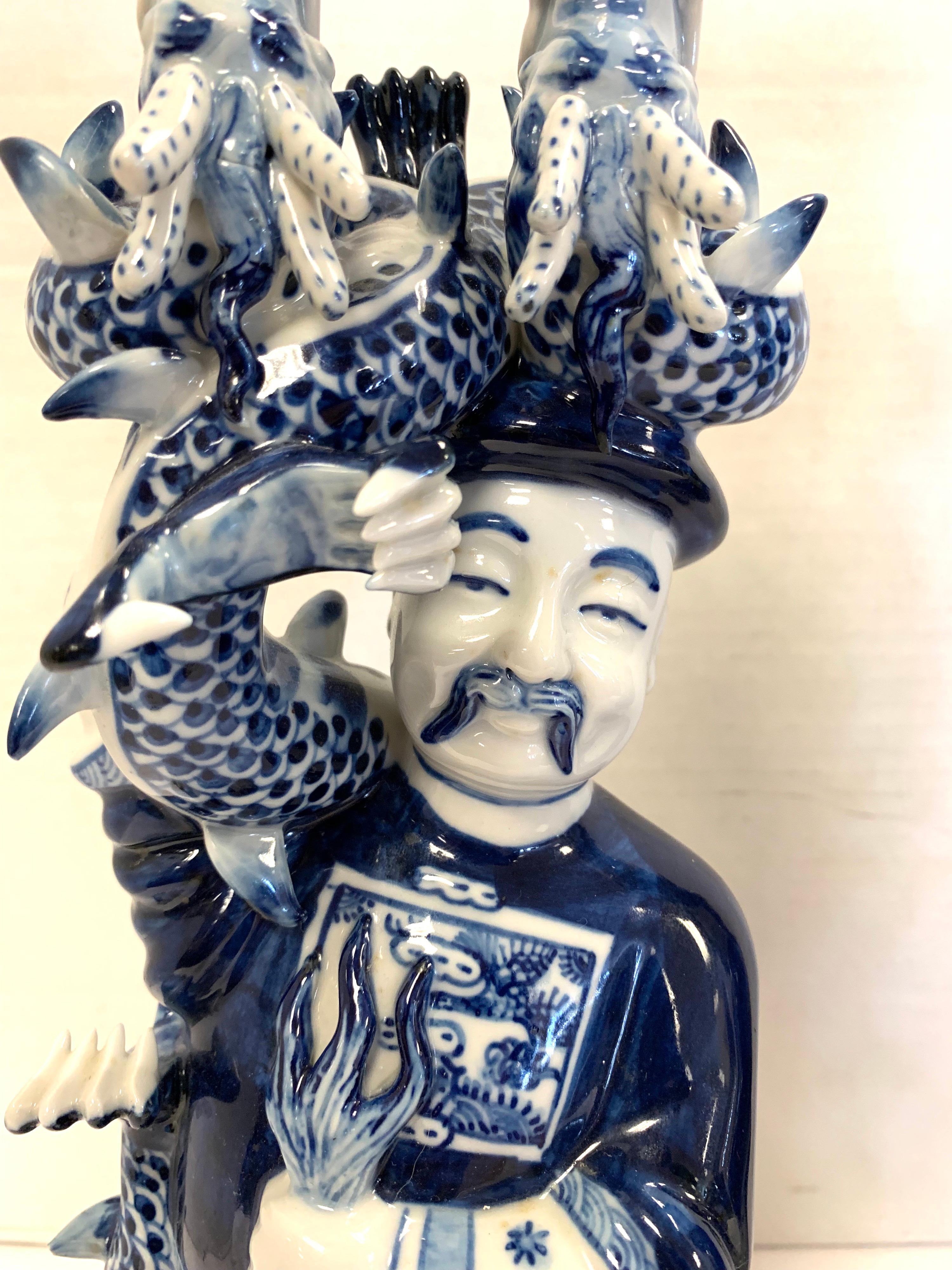 Stunning Chinese blue and white porcelain figural candleholders featuring an Asian man happily holding a two headed serpentine. Each hold two candles. These unique candlesticks will surely add character to your home.