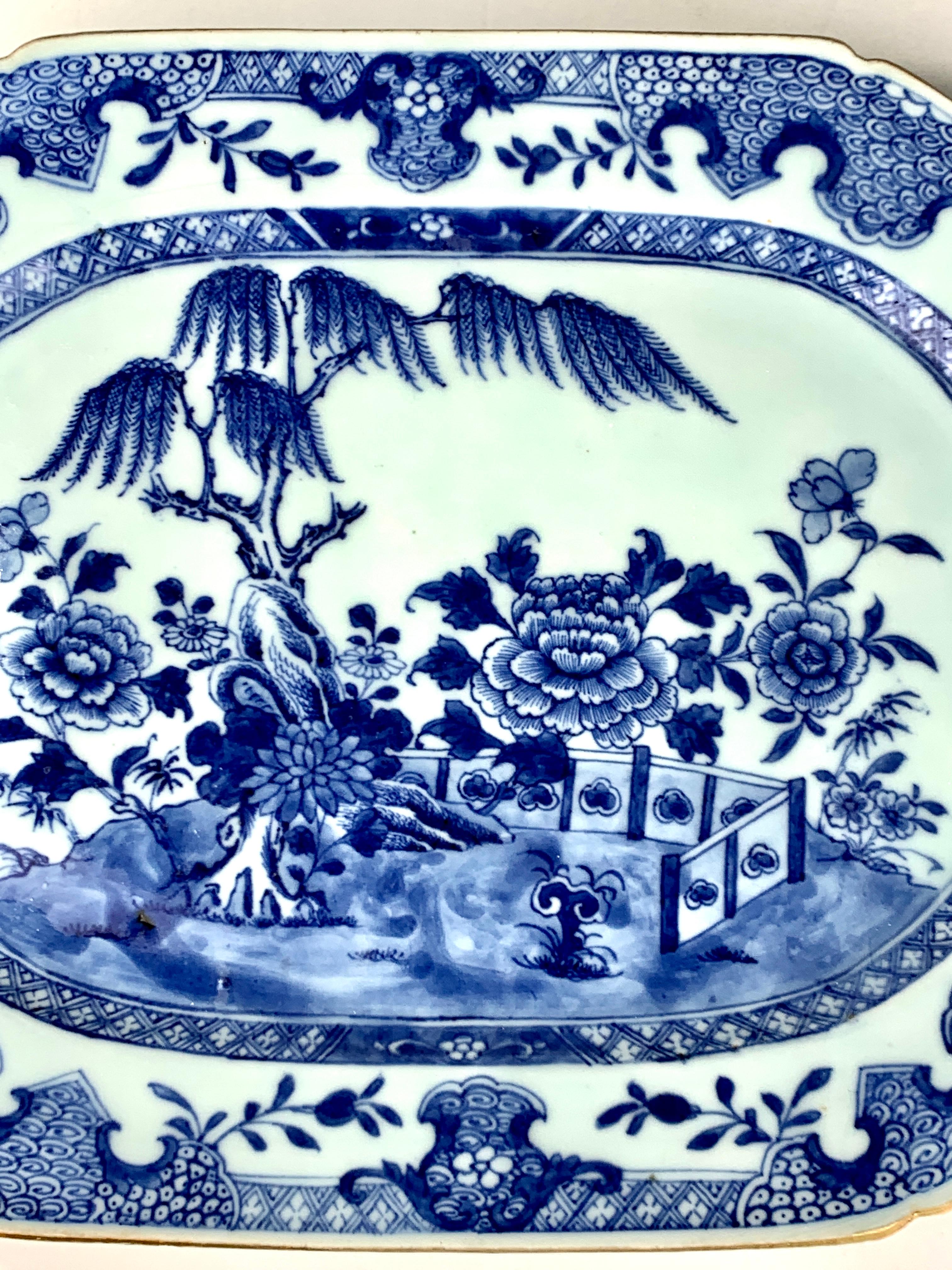 This exquisite Chinese blue and white porcelain platter was hand-painted in the Qianlong dynasty in the 18th century. It has the timeless appeal of beautiful flowers blooming in a garden. We see a fence, willow tree, rockwork, and large peonies,