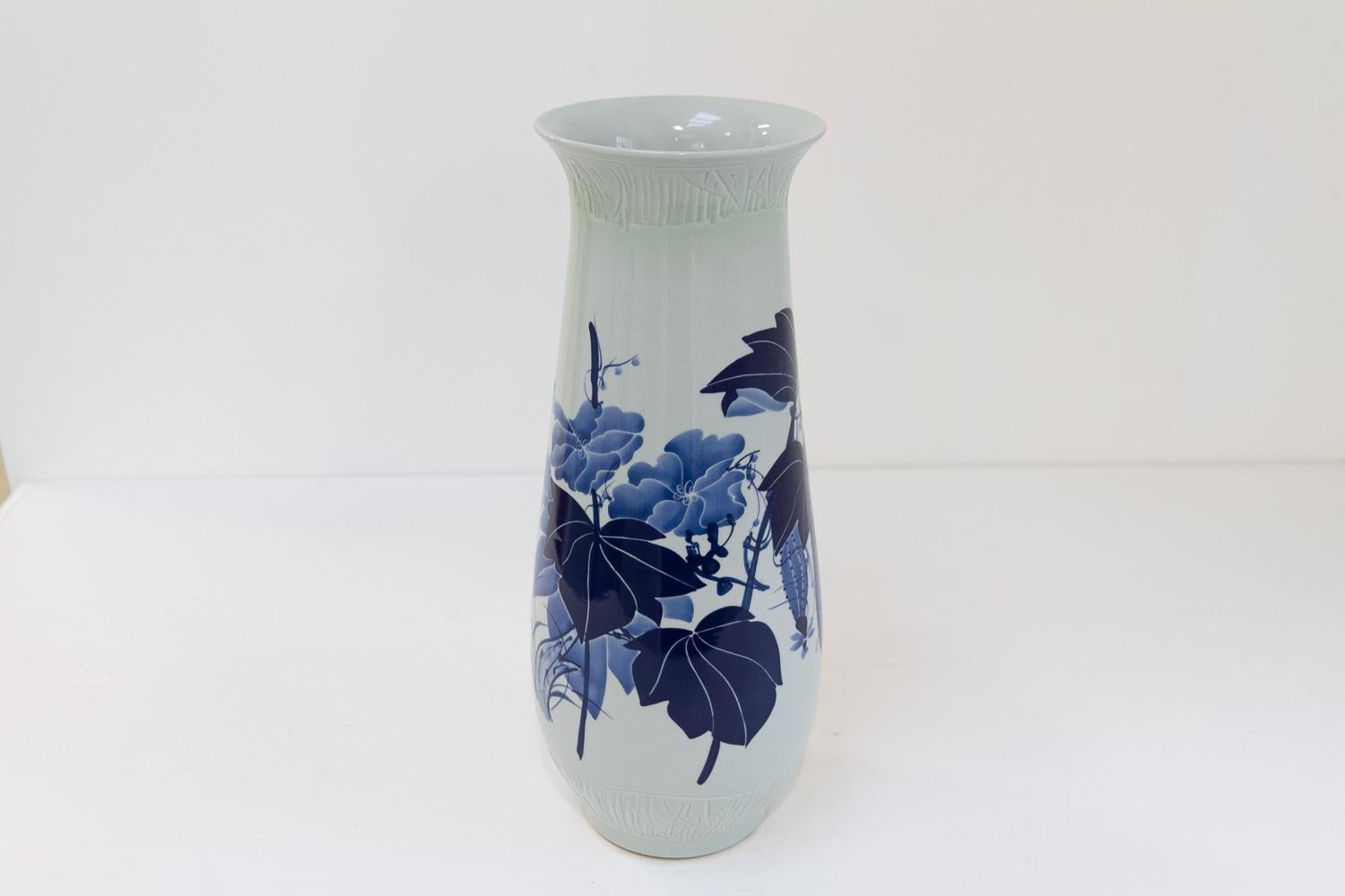 Vaso cinese in porcellana bianca e blu, anni '70.

Vaso cinese alto in ceramica smaltata e dipinta a mano con motivi floreali e calligrafia cinese decorativa in diverse tonalità di blu. 
Sezione trasversale ovale con parte superiore svasata.

Di