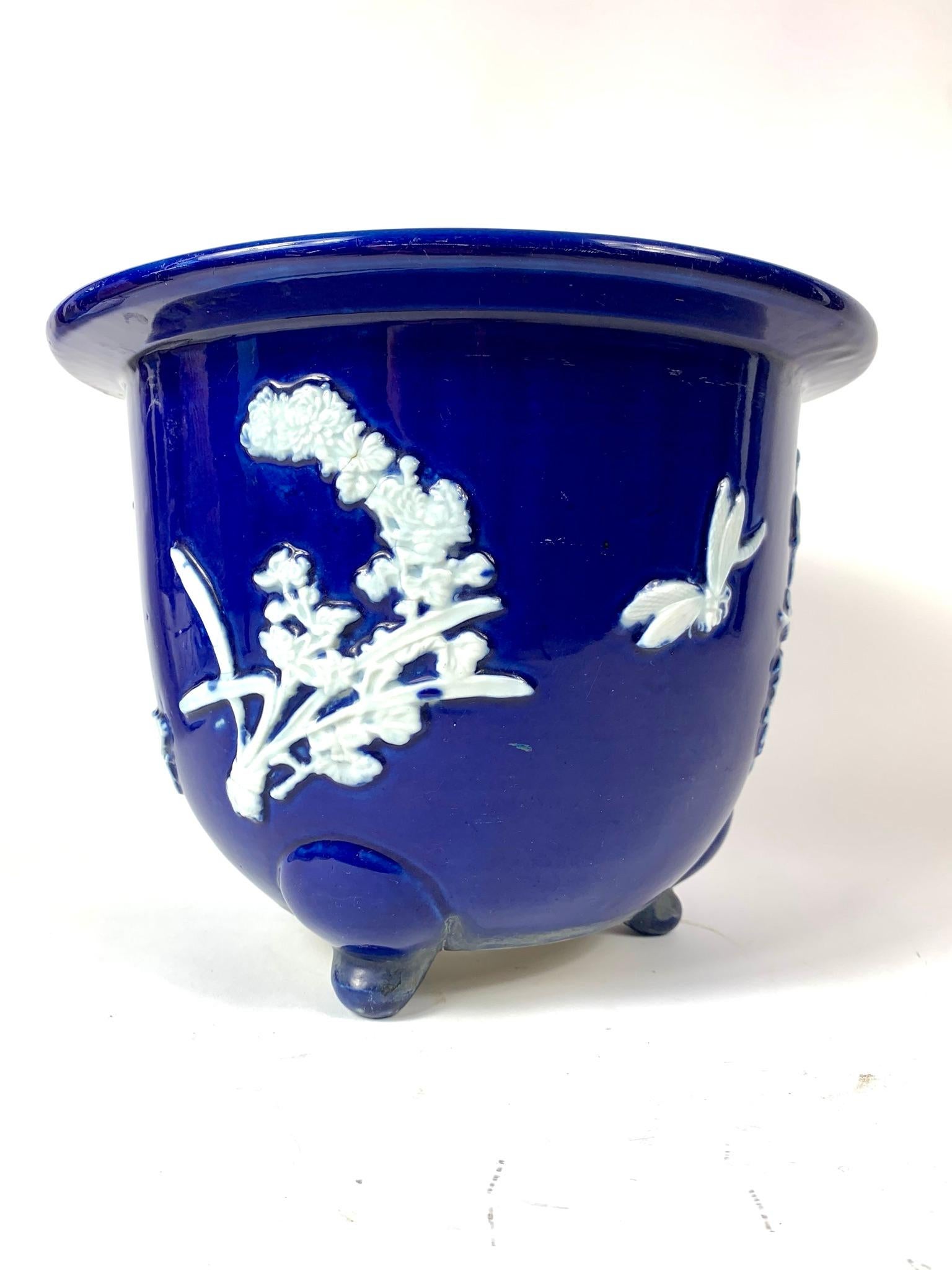 Chinese Pâte-sur-pâte jardinière in cobalt with raised white area decorated with flowers, butterfly and dragonflies. The bottom has three feet and a hole for water to drain through.

From Wikipedia:
Pâte-sur-pâte is a French term meaning 