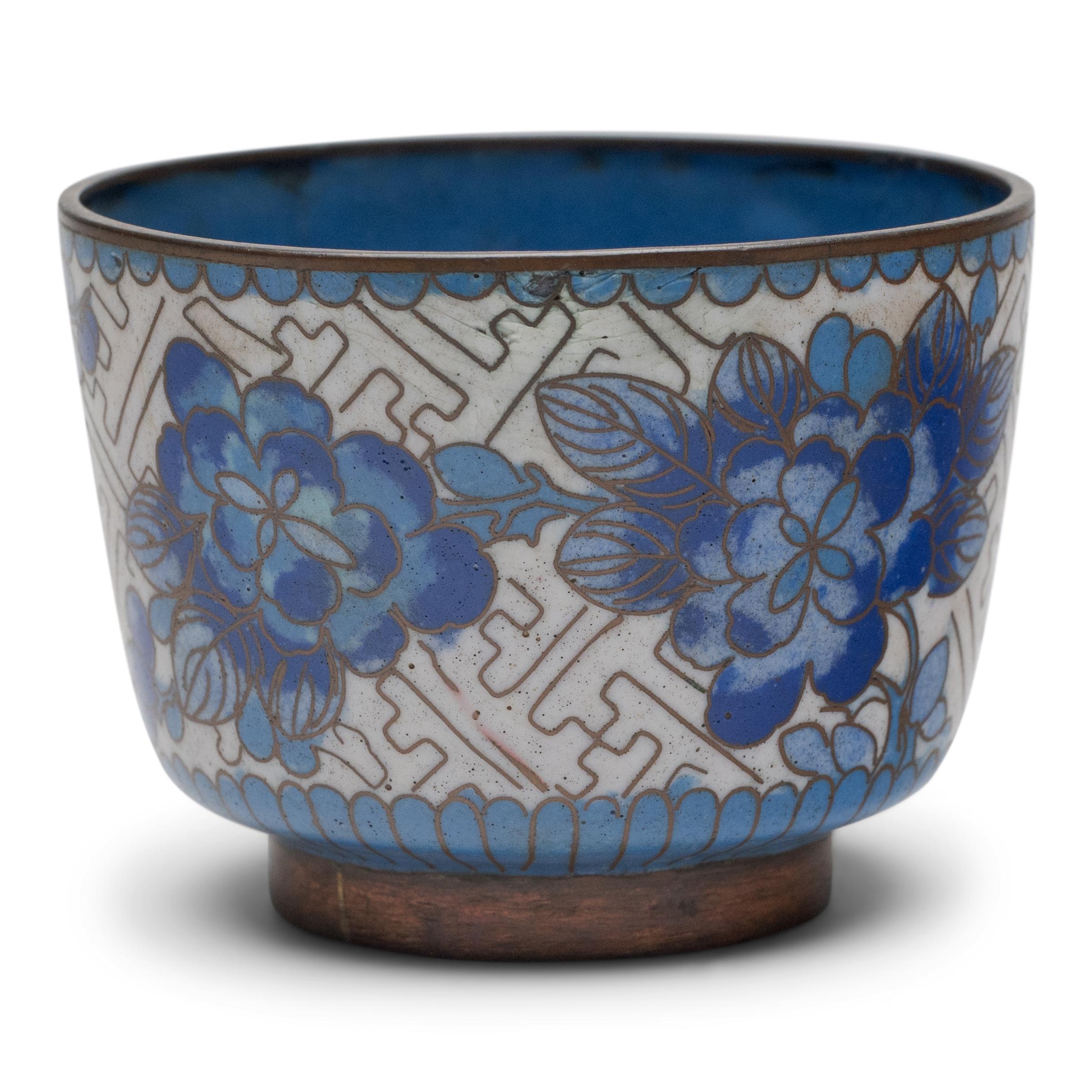 A matching set of Chinese cloisonné vessels, including one tea cup and one petite jar. Both cup and jar are decorated with softly shaded peonies and plum blossoms in a palette of blue and white enamels. The surrounding white field is patterned with