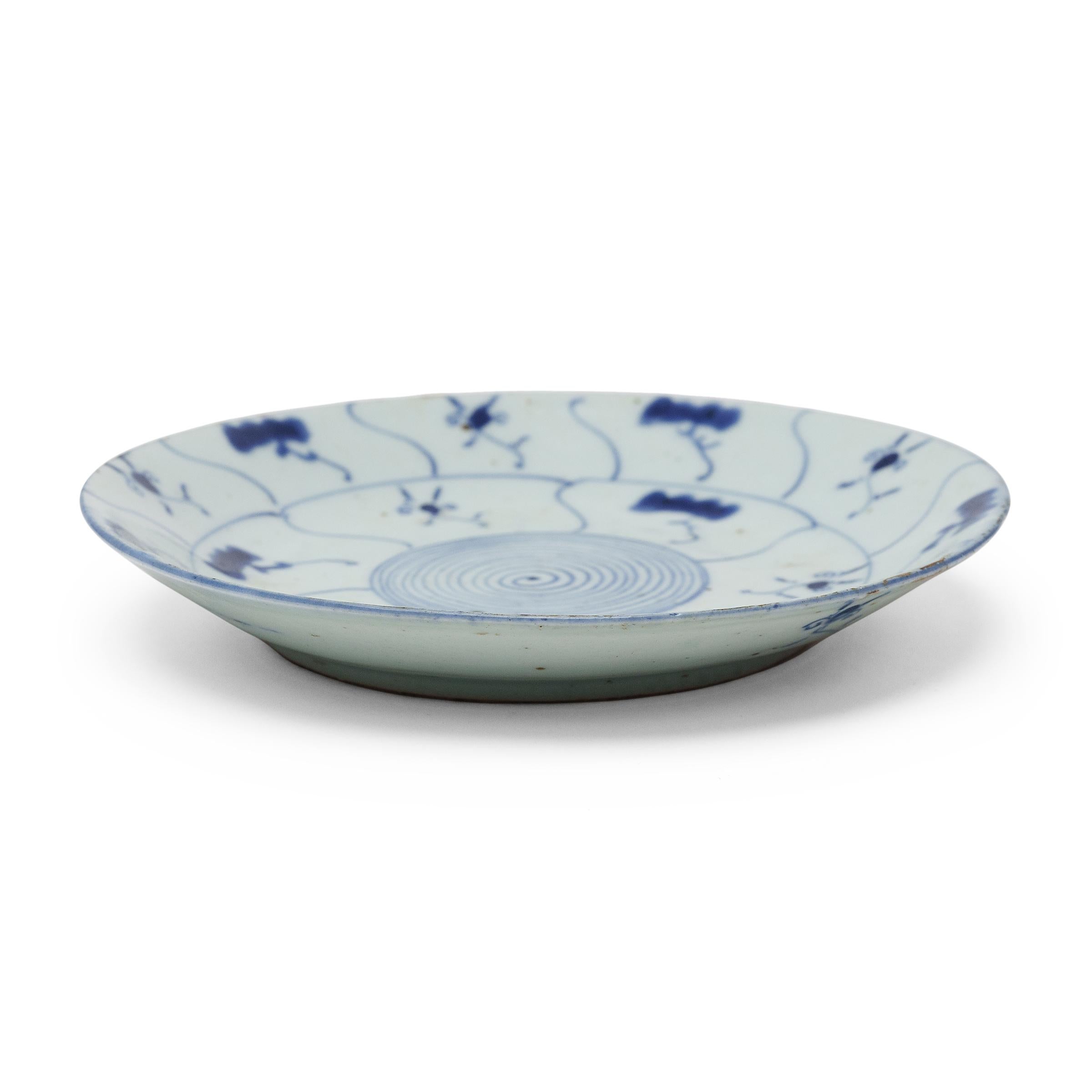 Este plato de porcelana del siglo XIX, ejemplo cotidiano de la porcelana china azul y blanca, destaca por su expresiva decoración azul cobalto, escasamente pincelada sobre un campo azul grisáceo. El plato redondo, con los lados suavemente curvados,