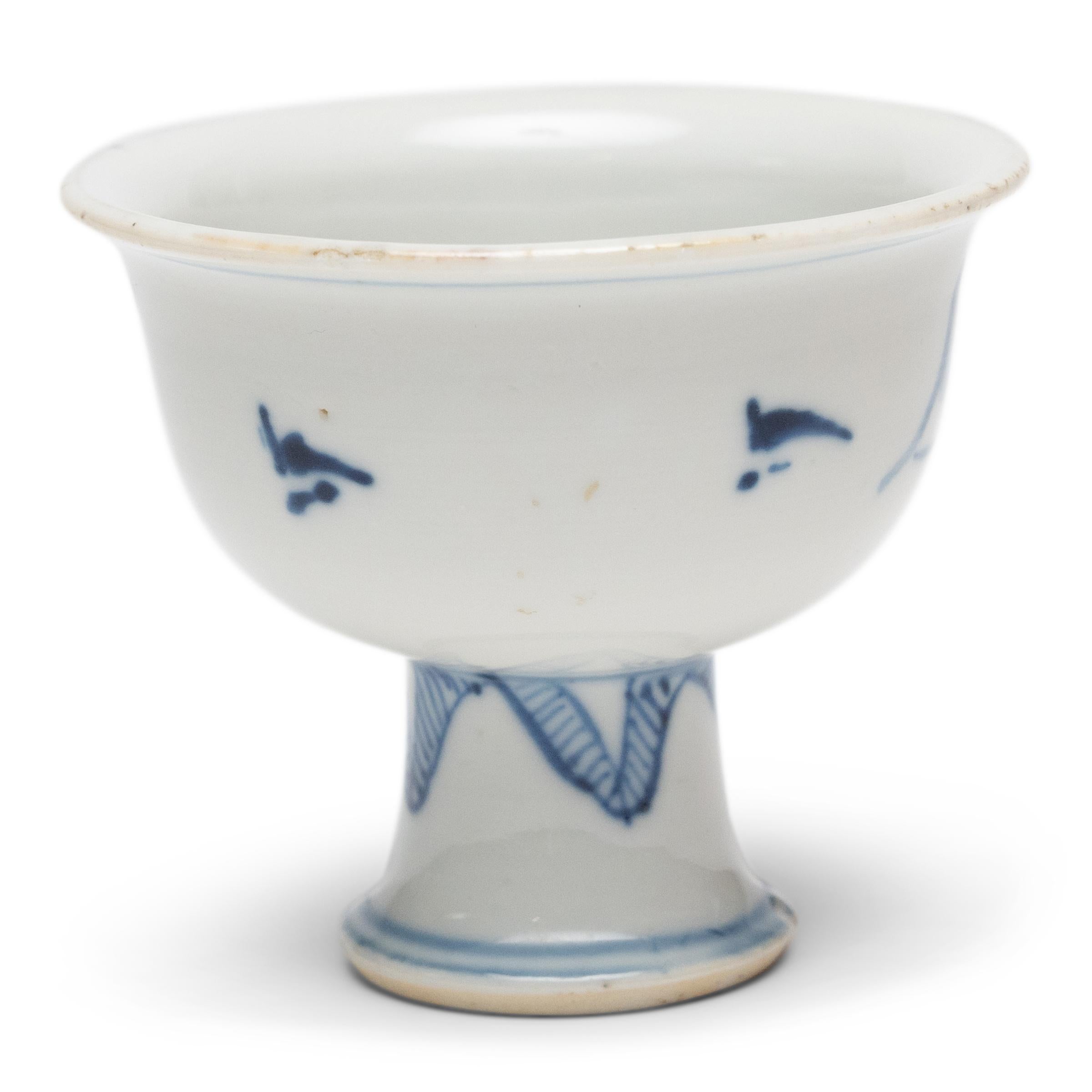 The delicate, blue and white design of this porcelain stem cup was painted in a muted, grey pigment, only to be transformed to a rich, cobalt blue by the fiery heat of the kiln. Elevated by a narrow stem base, the petite cup is decorated with an