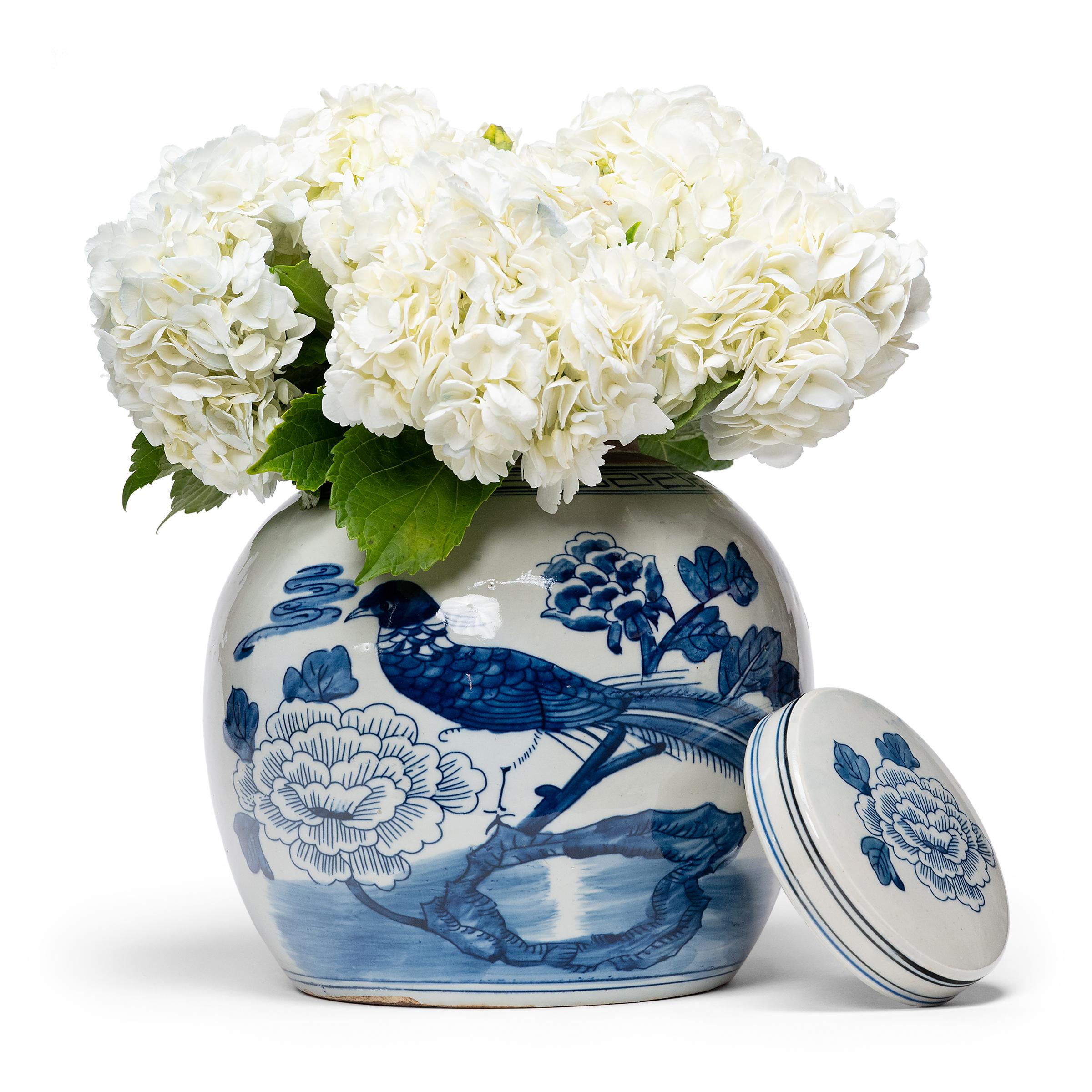 Loosely brushed with cobalt blue pigments, this round blue-and-white storage jar is adorned with a ribbon-tailed bird perched on a cluster of rocks, a symbol for a long and happy life. In combination with the surrounding peony blossoms, emblems of