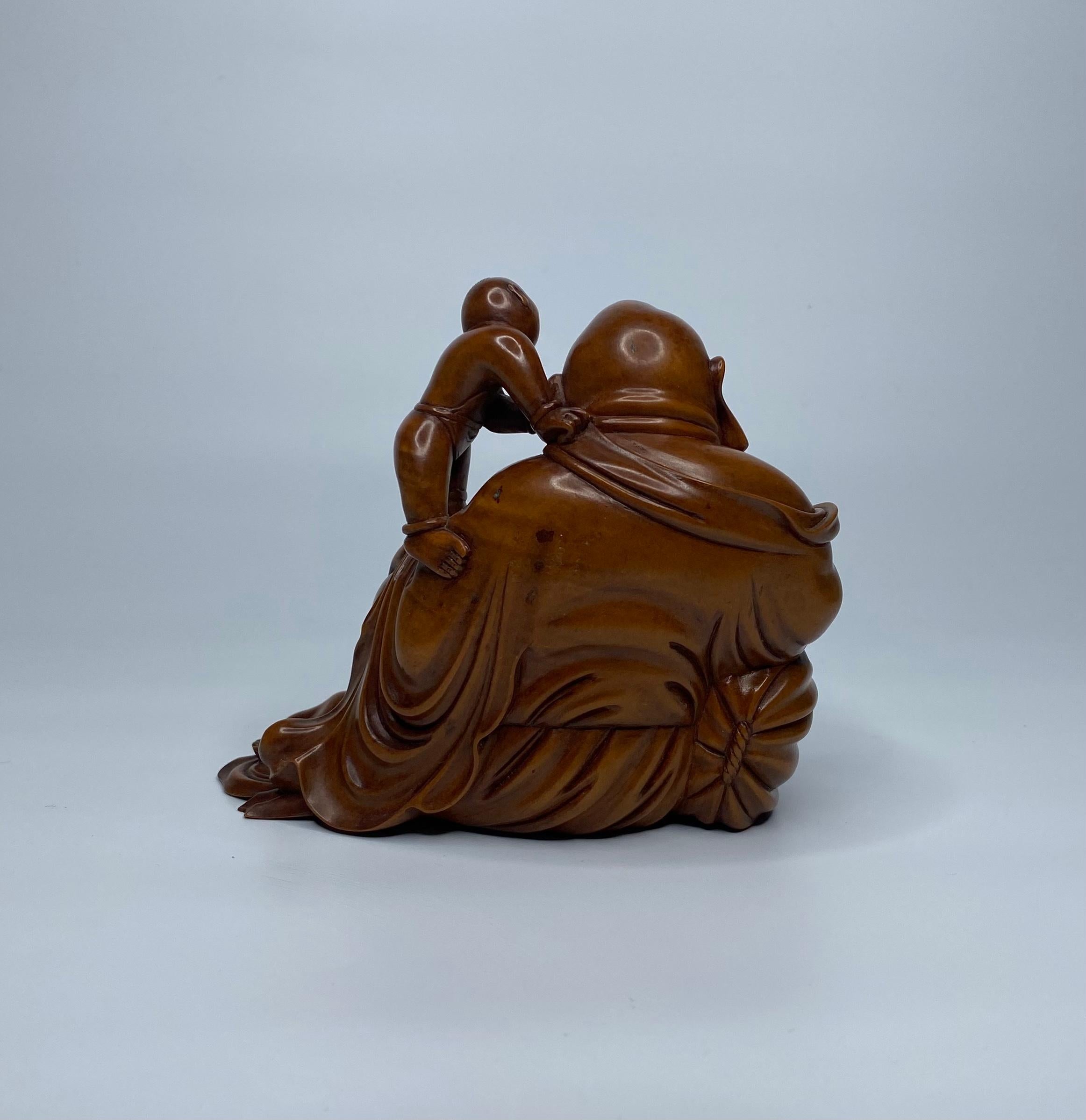 Chinese boxwood carved figure, c. 1900, Qing Dynasty. Finely carved as a smiling Buddha, being cleaned by two attendant boys. He wears flowing robes, and reclines against a large sack, whilst holding a bat, in his right hand. Having inlaid teeth and