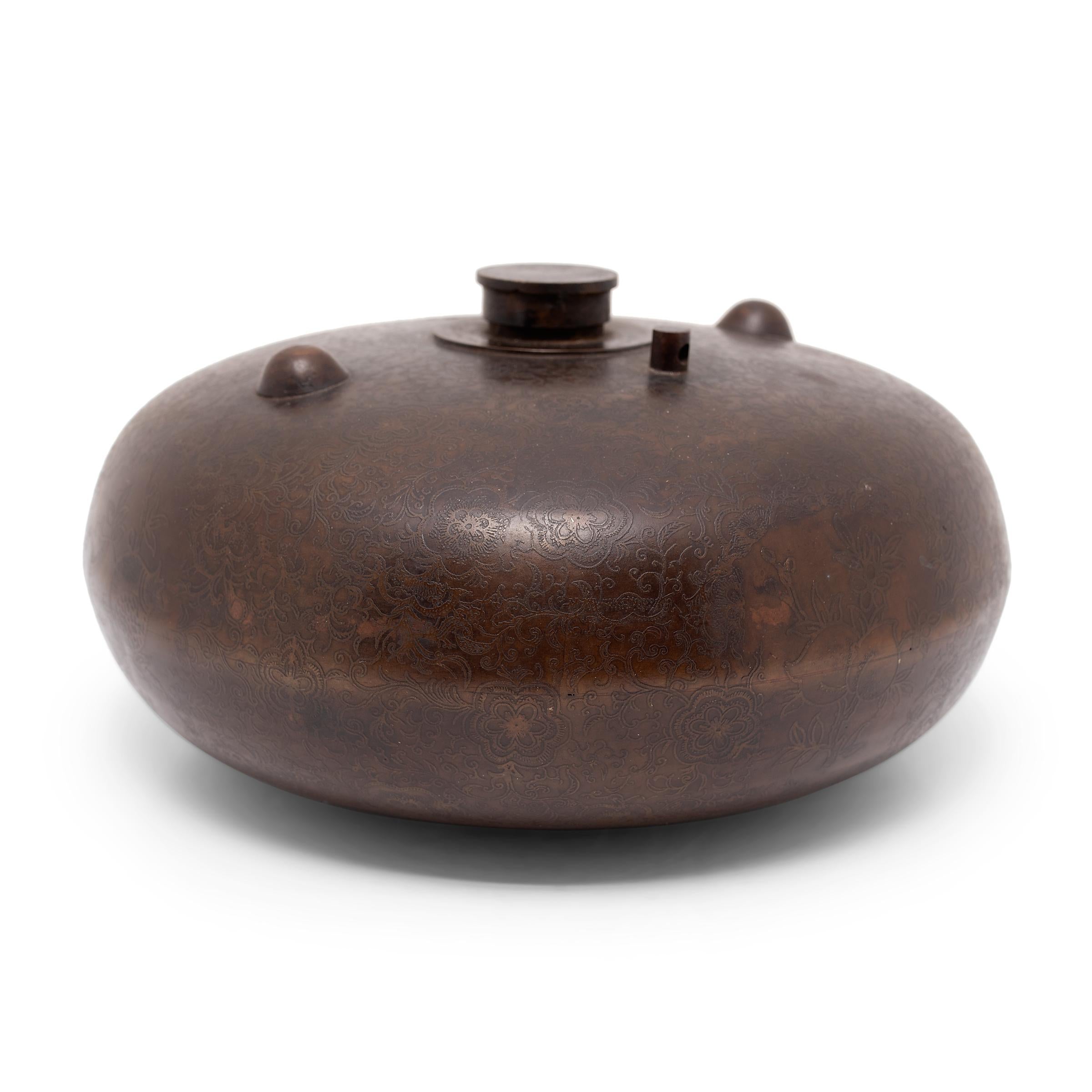 This squat brass vessel is an early Qing-dynasty hot water bottle, originally used to heat a bed or warm the body. The round container would have been filled with hot water through the narrow top opening and used to slowly radiate warmth. In