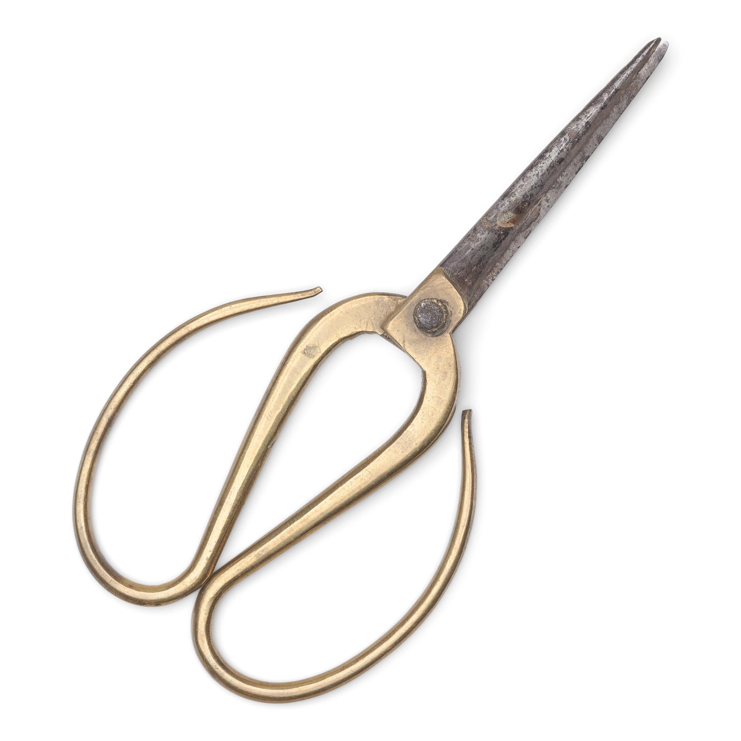An elegant pair of scissors once used to trim the wick of an opium lamp. The petite scissors are made of brass with polished handles that curve gracefully back towards the blades.