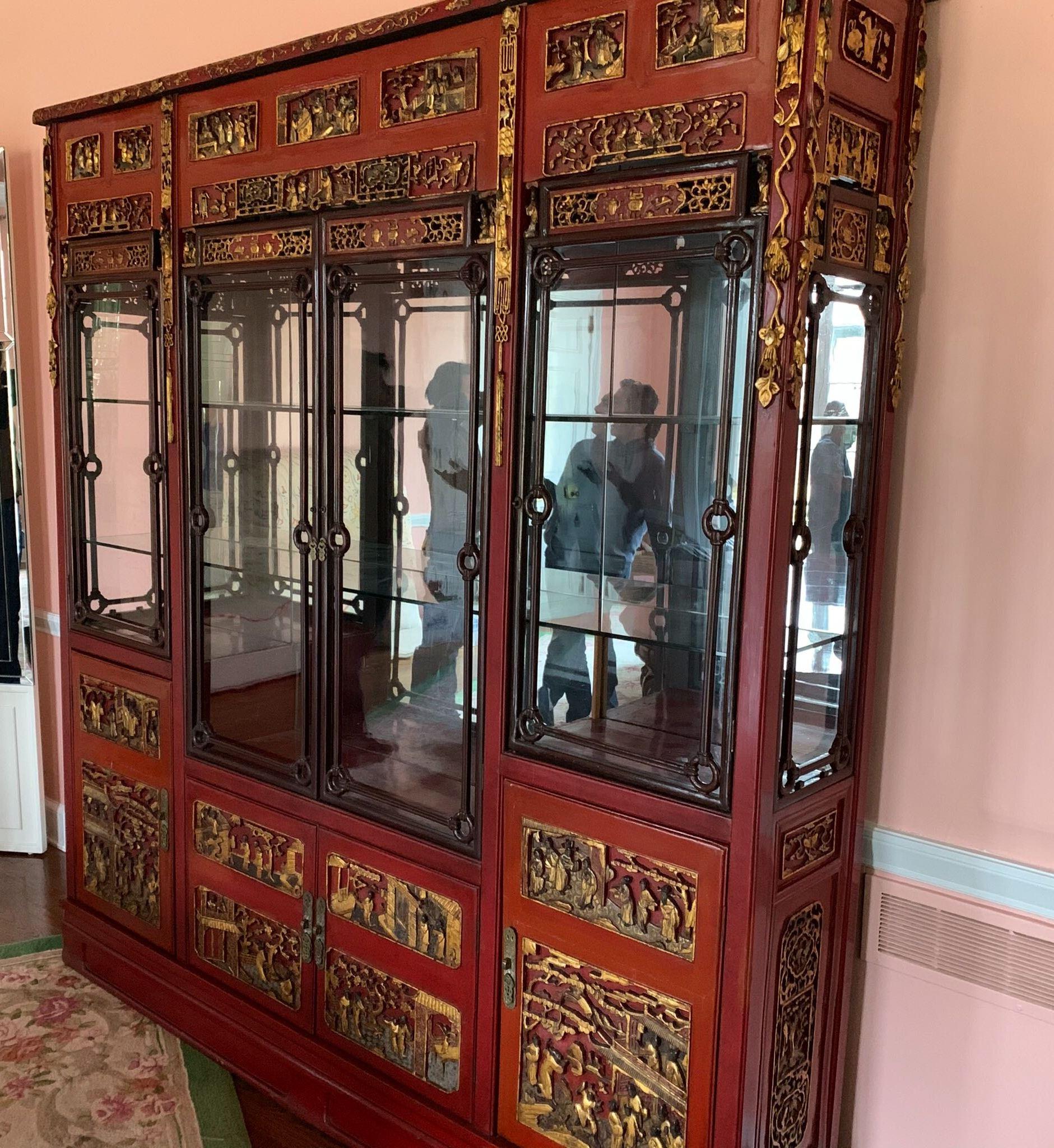Chinese breakfront cabinet in carved and partially giltwood with lacquered finish and mirrored back. The piece has four inset glass doors which open to three-glass shelves on the interior, over a four-door cabinet base with two-shelf interior. In