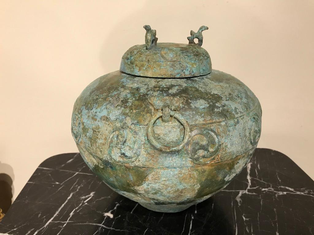 A bronze lidded ritual vessel modeled after a late Shang dynasty, circa 1600-1046 BC original. The lid and body of the vessel incised with bands of geometric and circular designs, all with an exceptional patina in varied shades of verdigris. The