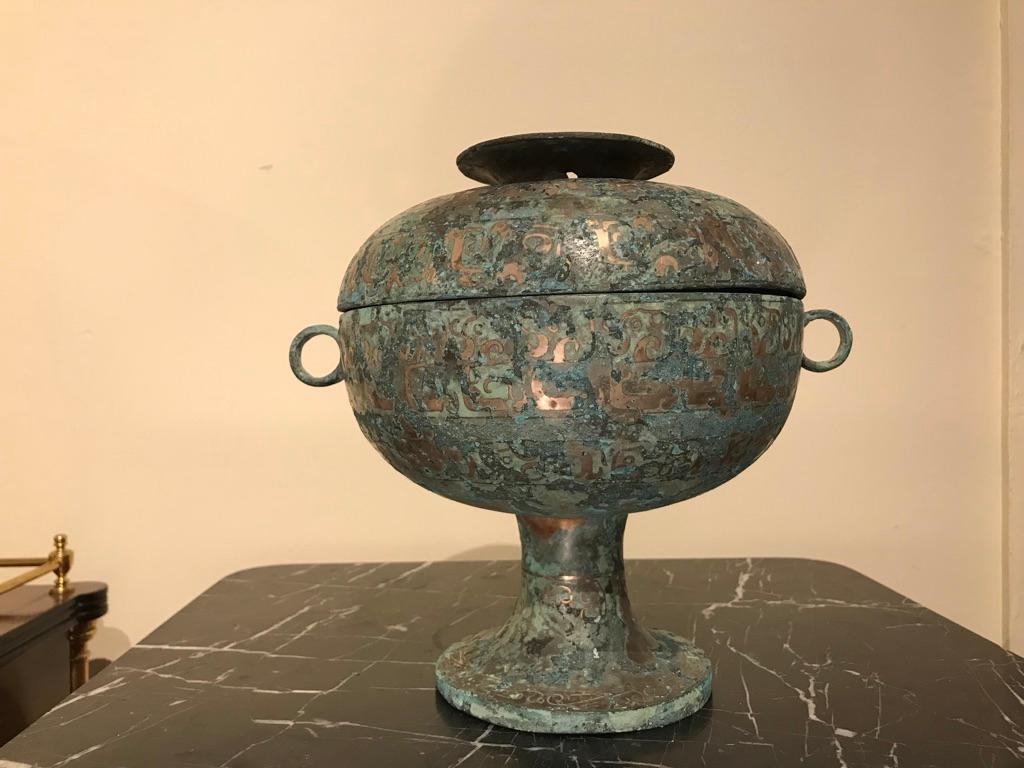 A Chinese silver inlaid bronze lidded ritual vessel modeled after a late Shang dynasty, 1600-1046 BC original. Of Classic form, with ring handles, the surface covered with inlaid Archaistic designs. The silver mixed with verdigris patina give this