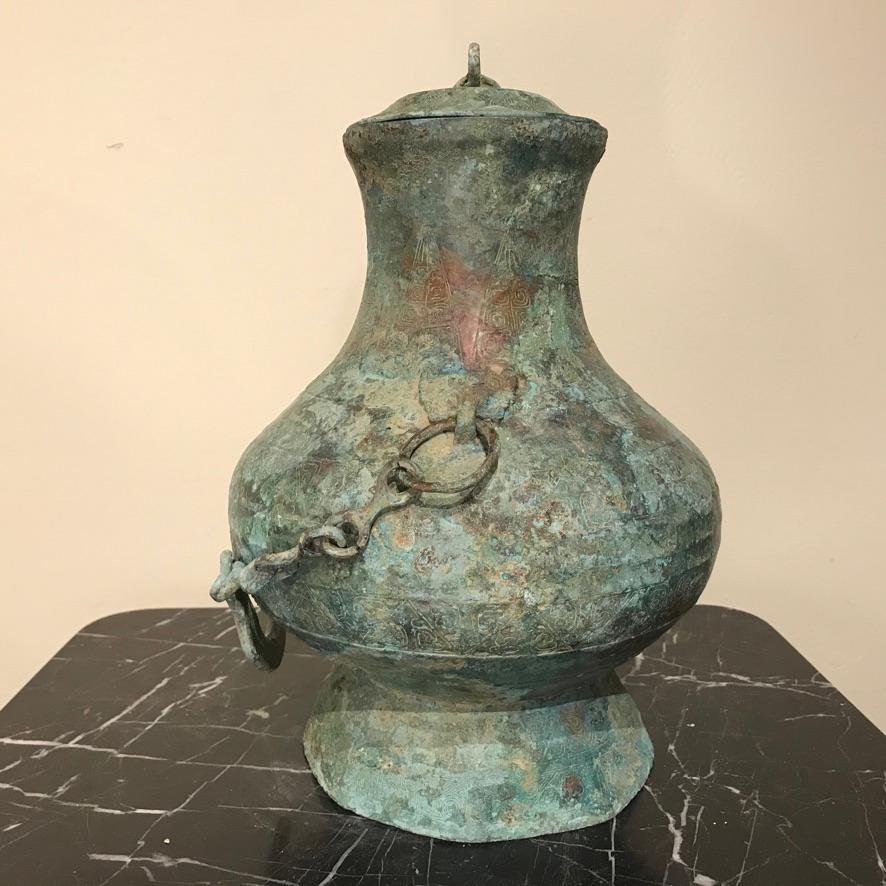 Unusual and very compelling Chinese archaistic lidded bronze vessel with handle attached with chain. Modeled after an original dating from the Warring States period, 2-3rd century BC. With incised ancient designs decorating most of the surface.