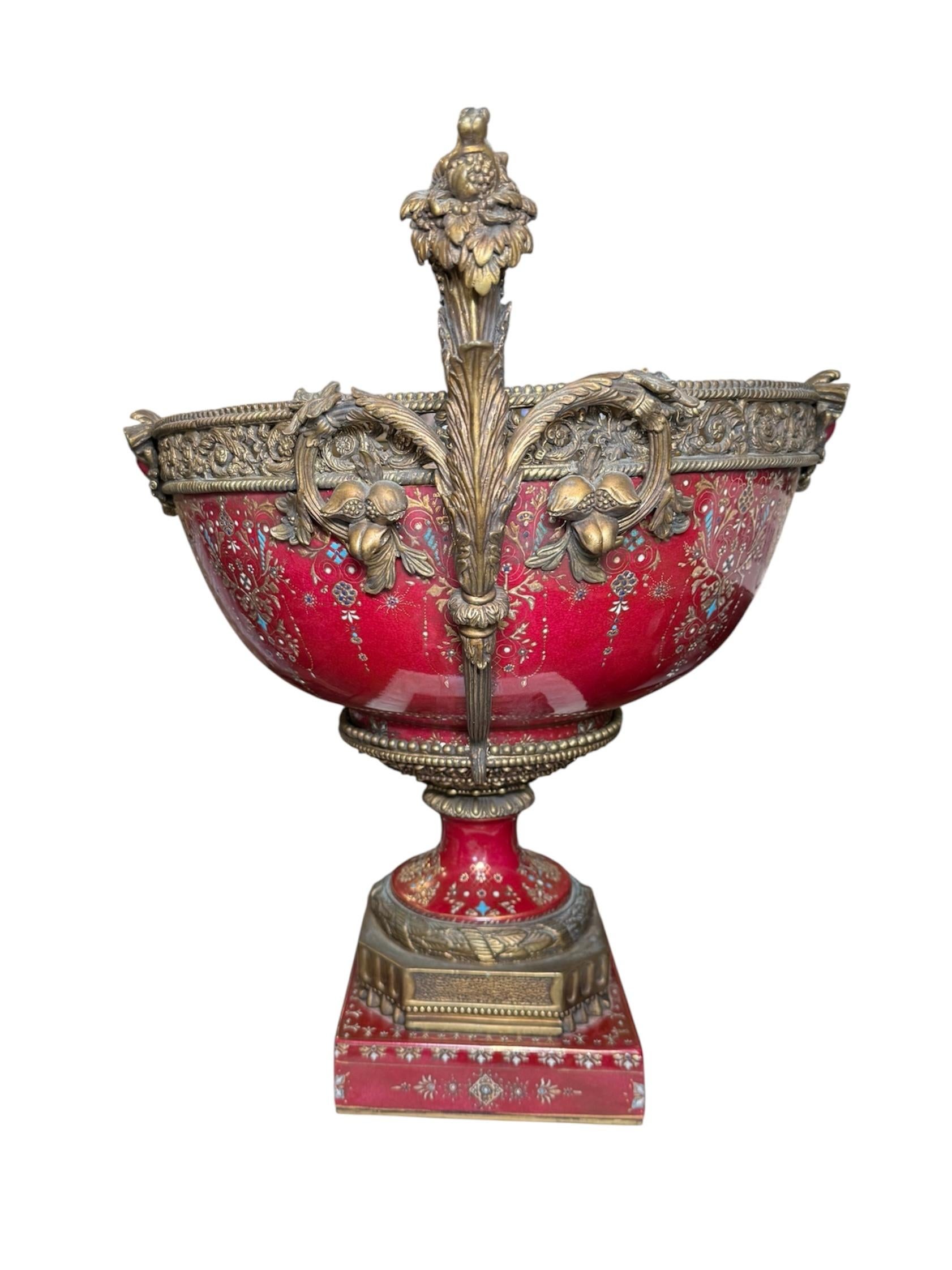 Si tratta di un centrotavola con piedistallo in porcellana color bronzo. Raffigura una coppa in porcellana pesante dipinta a mano di colore mirtillo rosso sullo sfondo e montata in bronzo. La porcellana è decorata con un motivo di volute dorate di