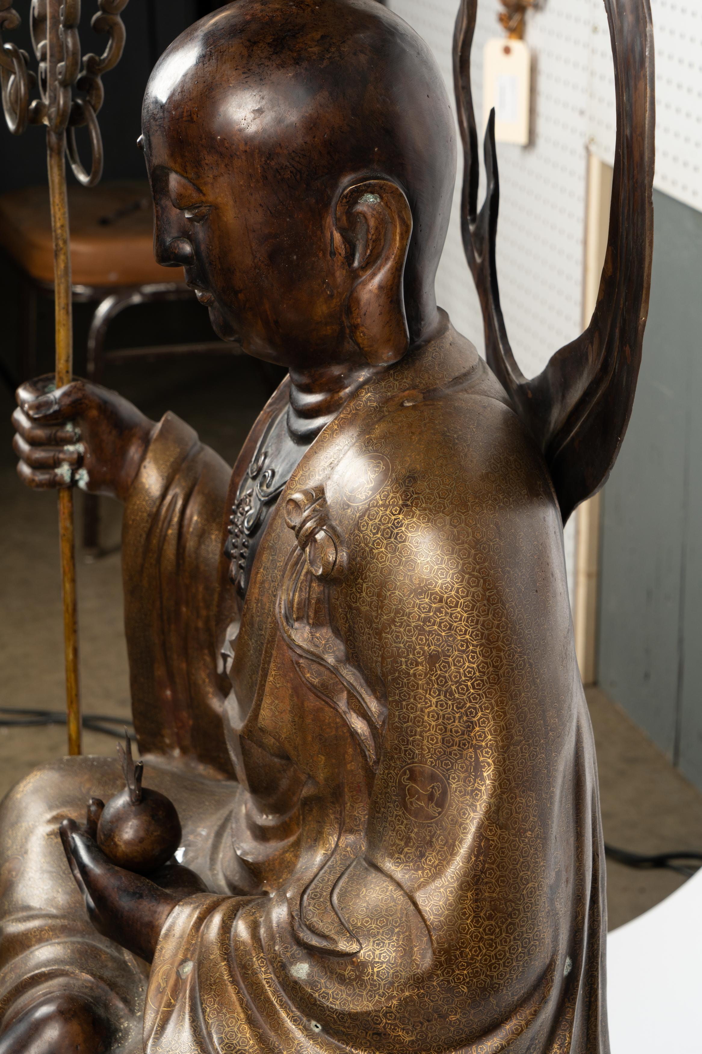 Chinesische Bronze sitzender Buddha Figur das Gewand mit gemusterten Dekoration. Der Stab, die Rückenplatte und die Feuerkugel in der Hand sind zum leichteren Transport abnehmbar.  Maße 58,5h x 24w x 17d
