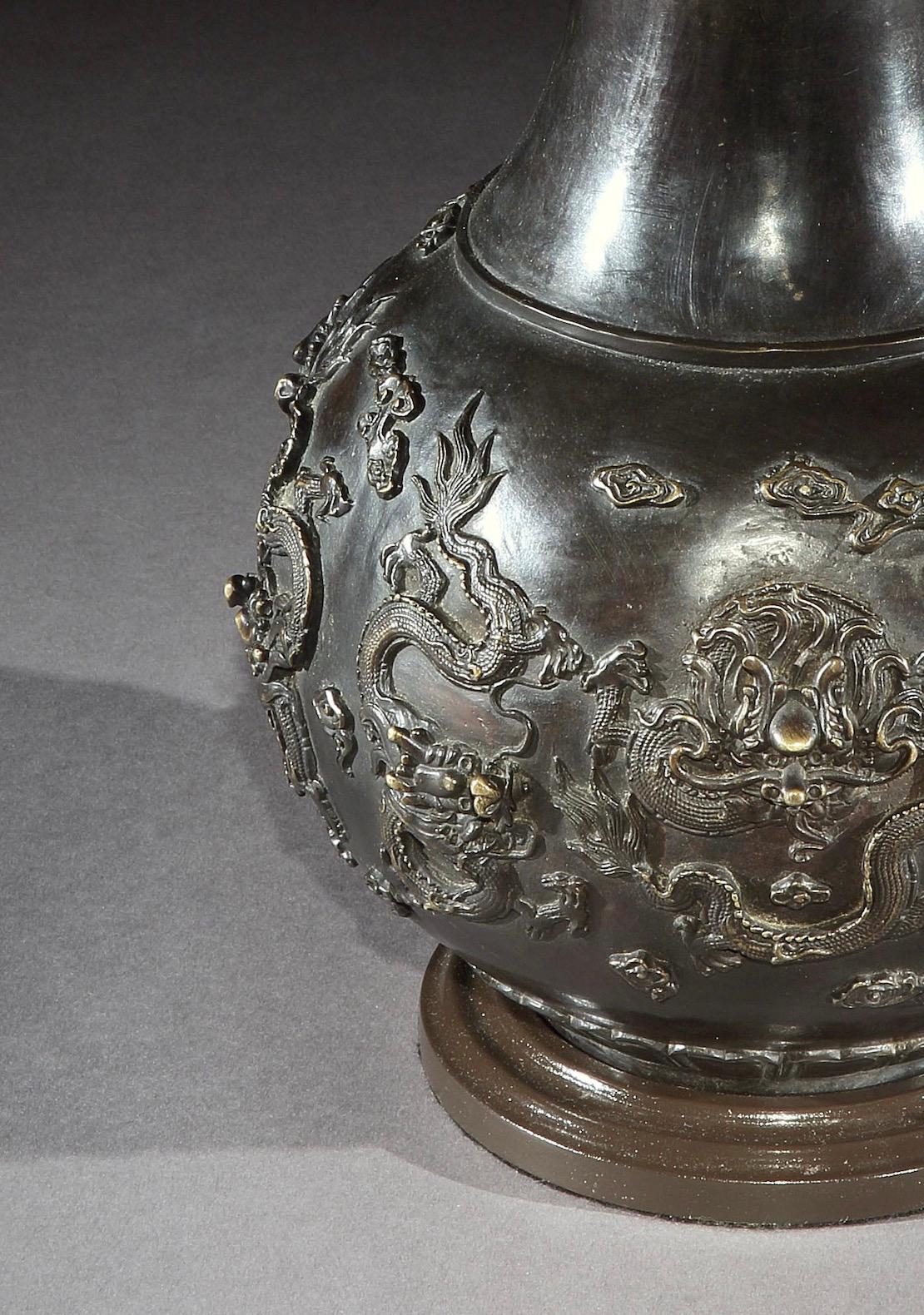 Un vase chinois en bronze présente une décoration appliquée de quatre dragons chassant la perle flamboyante. Maintenant monté comme une lampe.

Hauteur du vase : 16½ po (42 cm) incluant la base, excluant les installations électriques et les