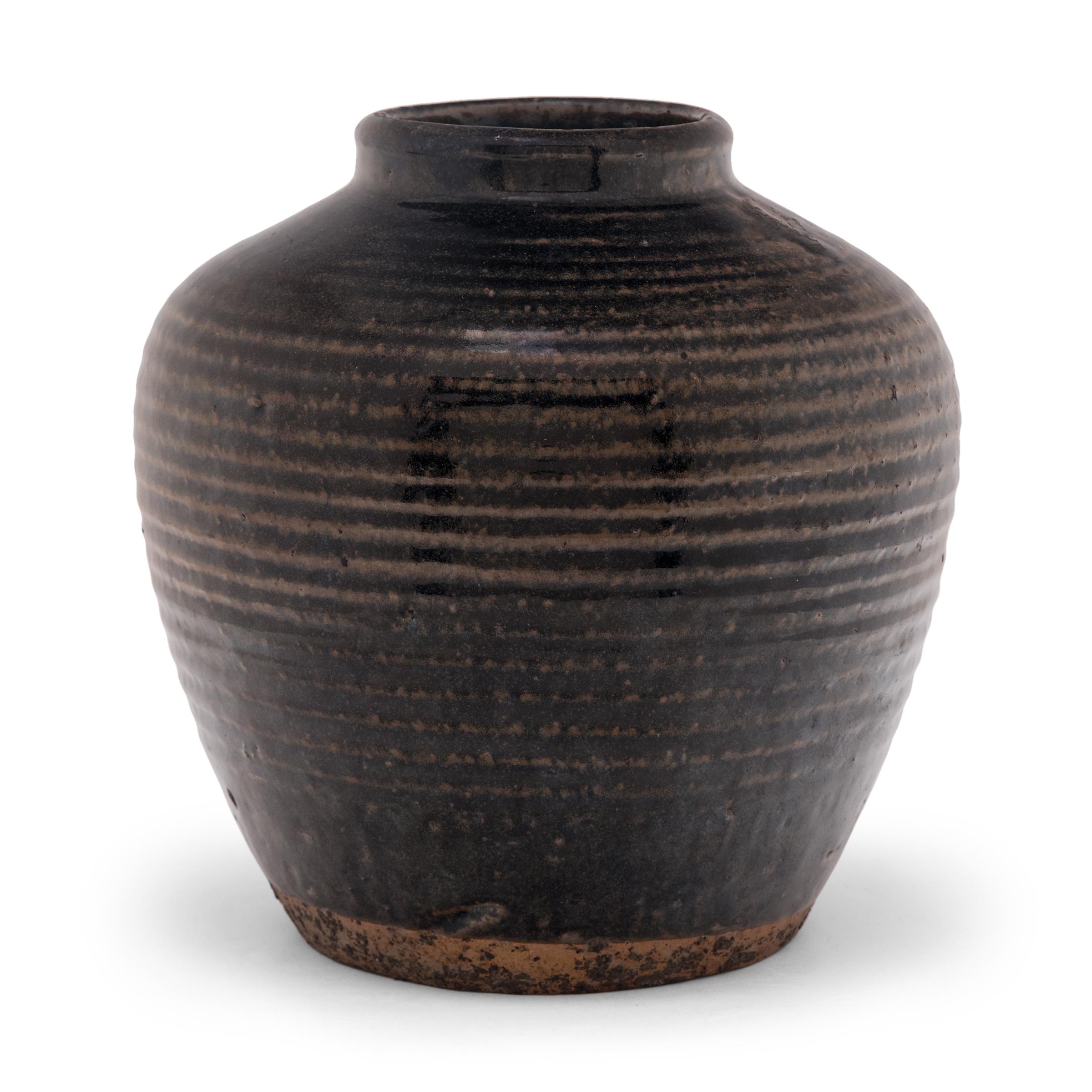 A dark brown glaze clings to the textured surface of this wine jar, lingering on subtle ridges ringing the body to create a pattern of light and dark. As evidenced by the interior glaze, the jar was once used to store wet foods in a Qing-dynasty