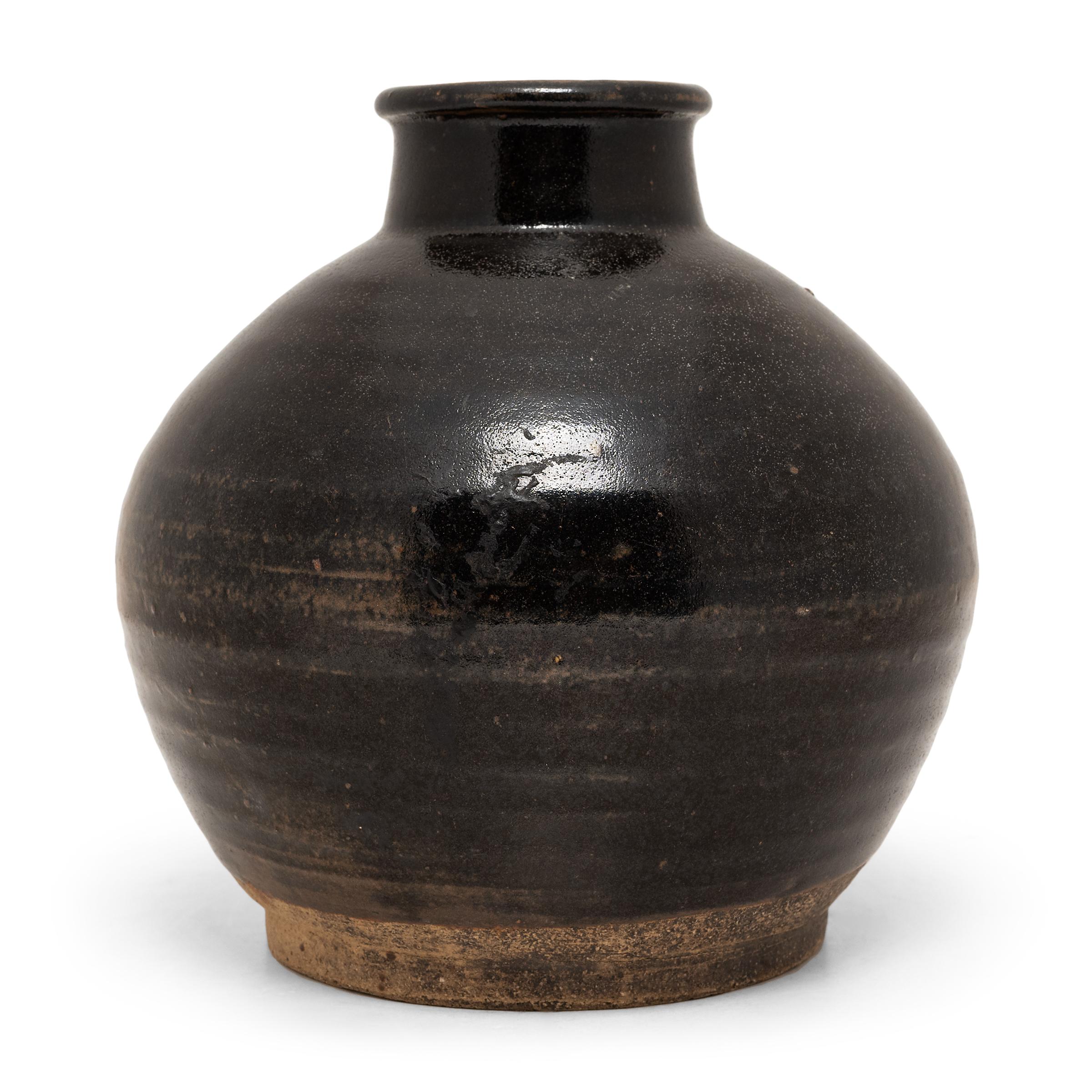 A rich brown glaze coats the surface of this round wine jar, lingering on subtle ridges ringing the body to create a pattern of light and dark. Crafted in the early 20th century, the jar was once used in a Qing-dynasty apothecary to store wines