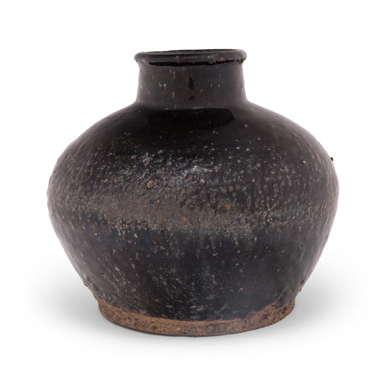 A dark brown glaze coats the surface of this round bottleneck jar, beautifully textured by pitted wear and contrasted by the unfinished base. Crafted in the early 20th century, the jar was once used to store liquids such as soy sauce, vinegar, and