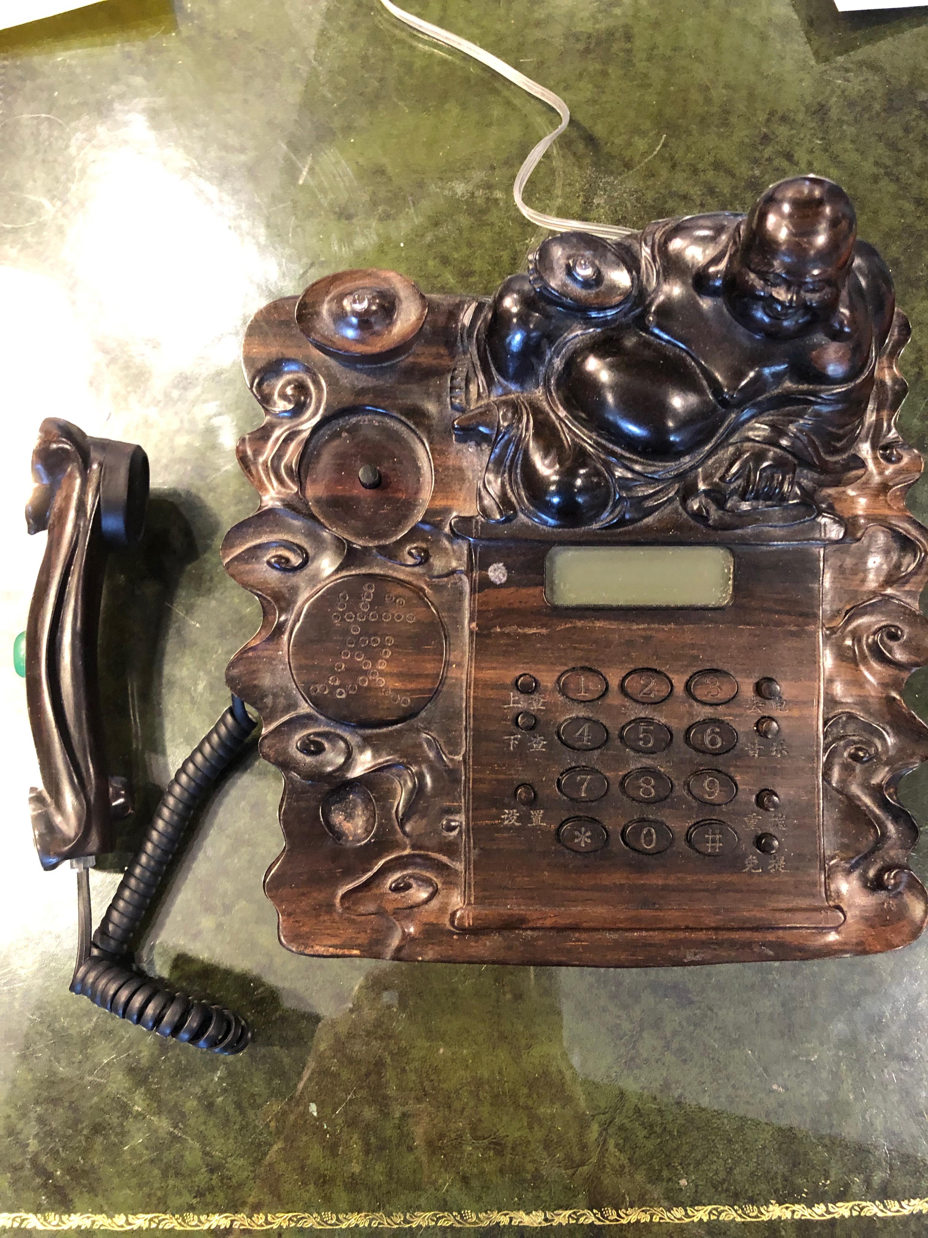 A very unique item! A hand carved mahogany Chinese Buddha telephone having a green jade embellishment on the carved handle to the left side of the Buddha. English numbers on each button.