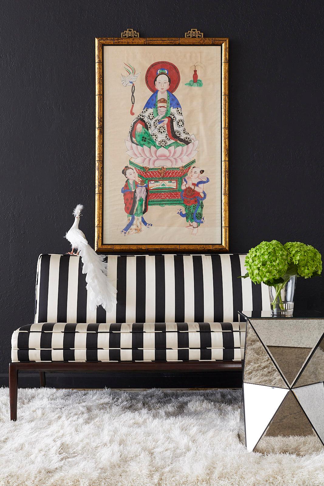 Colorful Chinese Buddhist Bodhisattva painting of Guanyin depicted sitting on a lotus blossom with two attendants. Ink and color pigments on paper set in a faux bamboo giltwood frame. The frame has a lovely distressed finish topped with brass