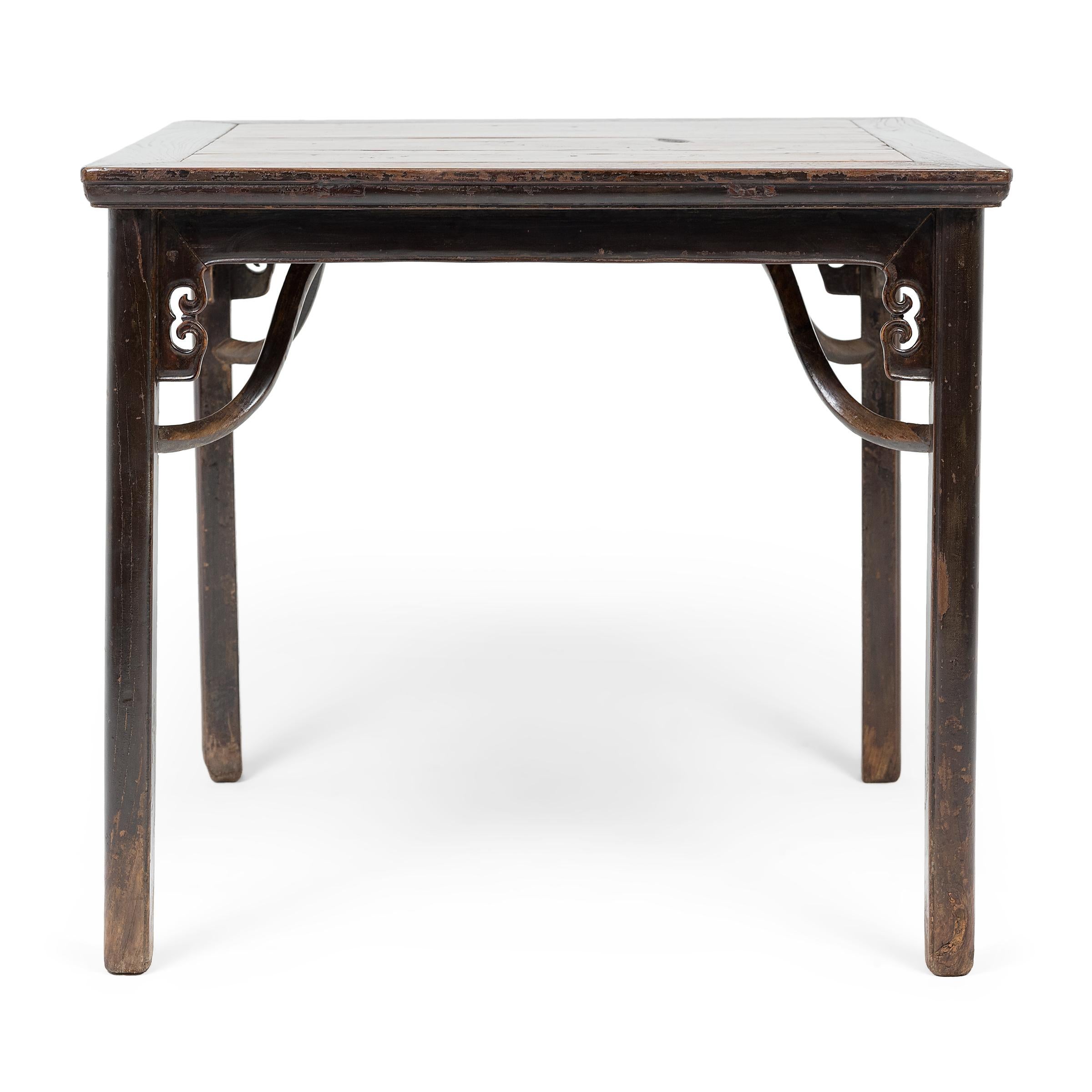 This early 19th century square table from northern China expresses Ming-dynasty tastes with clean lines and a simple silhouette. The table stands on four straight legs stabilized by giant’s arm braces and topped with scrolled spandrels carved in the