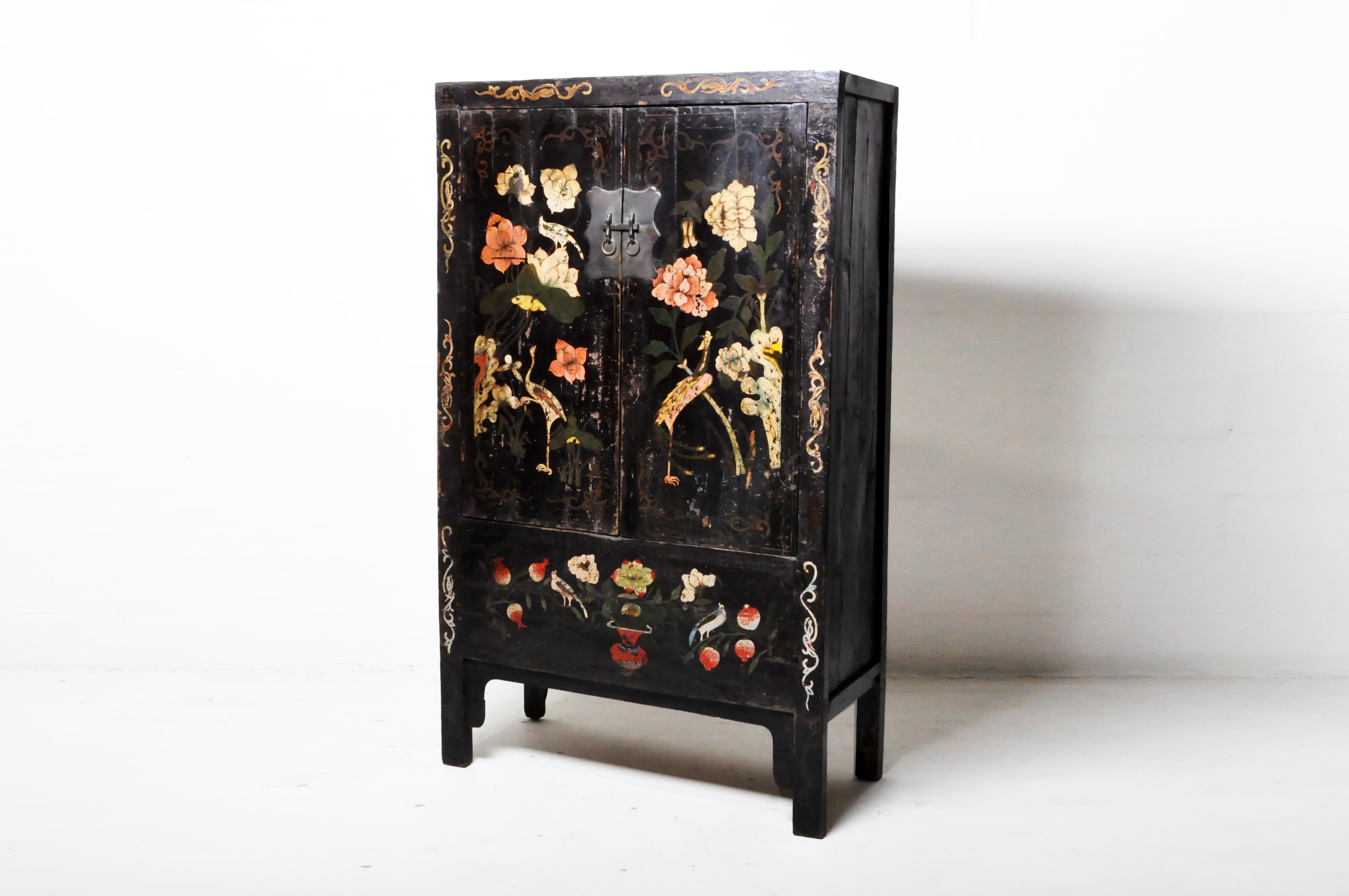 This Chinese cabinet was made in China and was made from elmwood with traditional nail-less joinery, c. 20th Century. The piece features two doors, two shelves, and floral and bird artwork. Wear consistent with age and use.
 