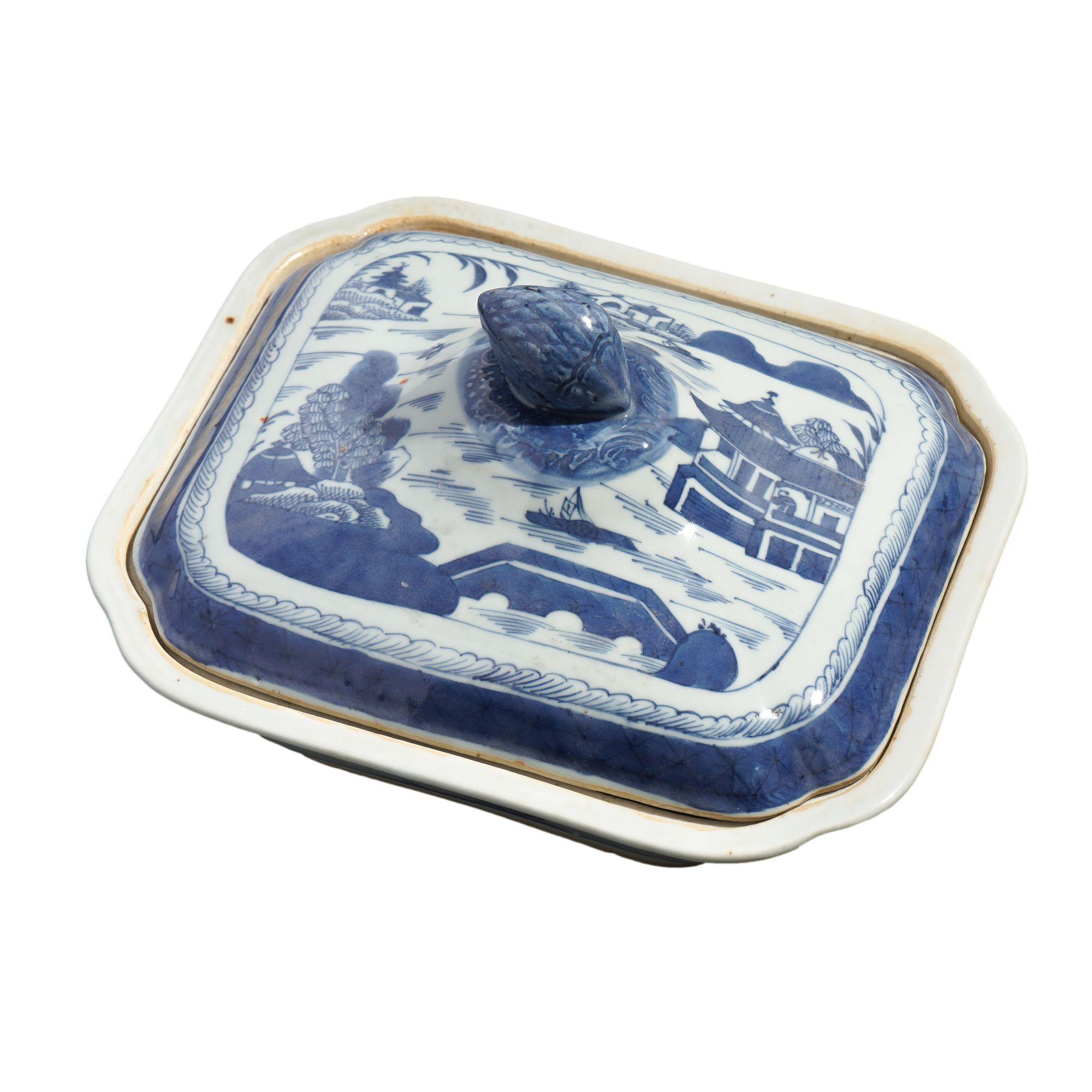 A square Canton porcelain covered entree dish with dimpled corners. The decoration is in cobalt underglaze blue with a willow tea house pattern. The dish has a flaring rim with an inset for the domed cover with finial. The tea house decoration is
