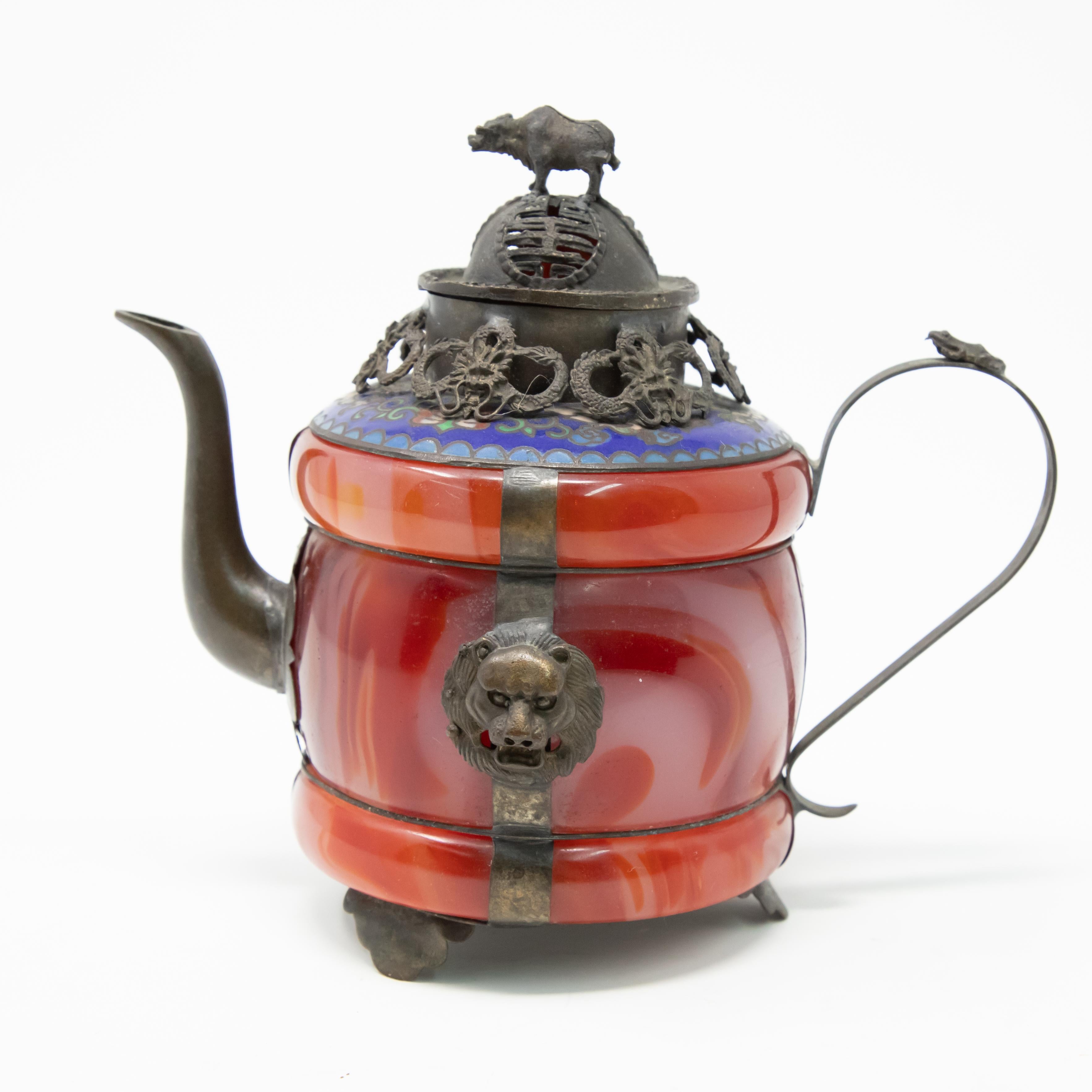 Offering this unmatchable Chinese teapot made of carnelian stone with enameled bronze and filigree. Starting on a footed bronze base the carnelian stone is attached with bronze bands to the base. Off of one of the bands the handle is attached with a