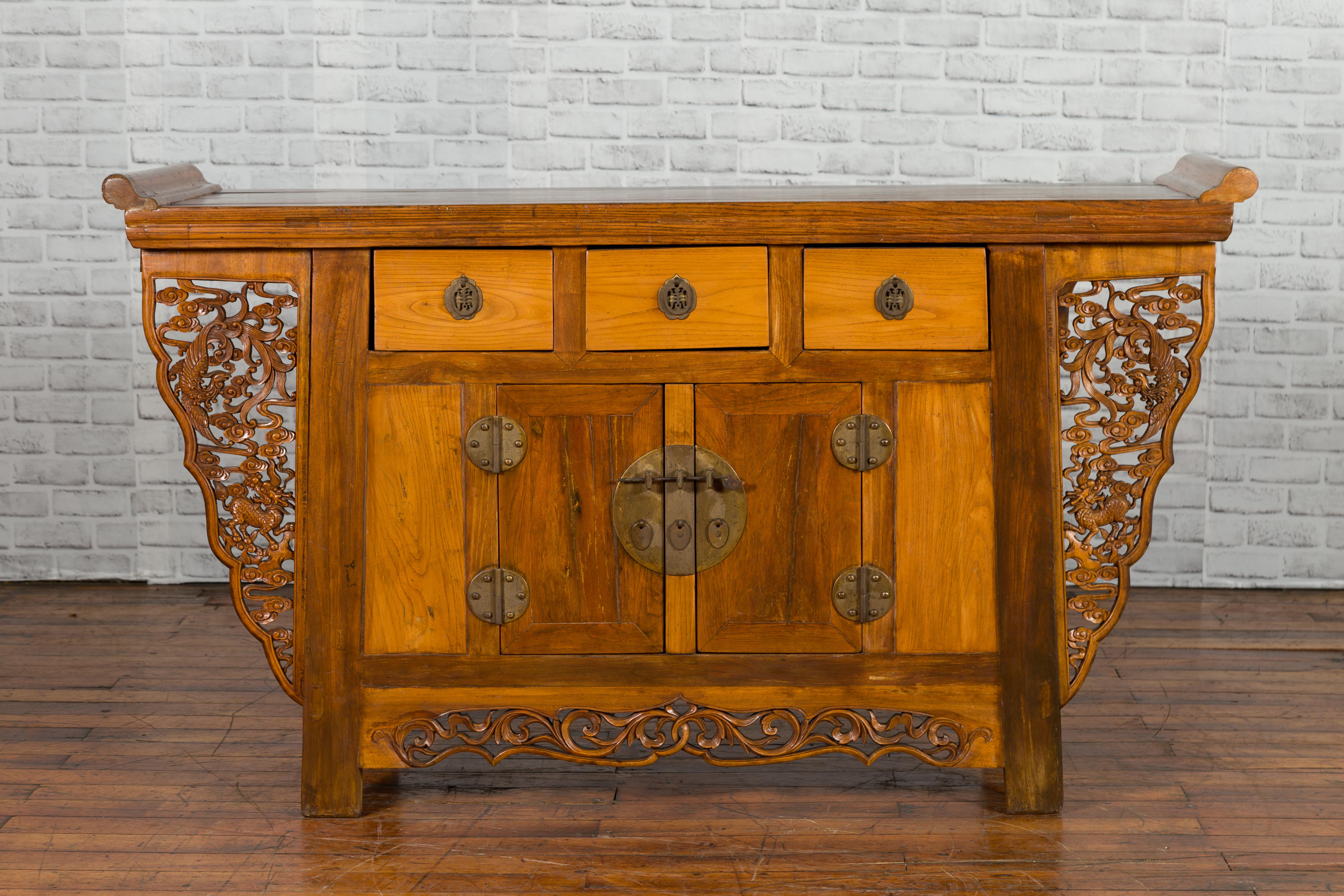 A Chinese Qing Dynasty period altar console cabinet from the 19th century with everted flanges, three drawers, petite double doors and carved spandrels with mythical animals. Created in China during the Qing Dynasty period, this altar cabinet
