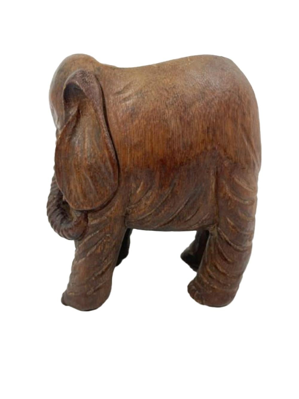 Vasija de bambú tallado en forma de elefante de pie, con la trompa curvada hacia un lado y las patas ligeramente dobladas hacia dentro, siguiendo la forma natural de la pieza de bambú. La parte superior de la vasija se ha dejado abierta formando una