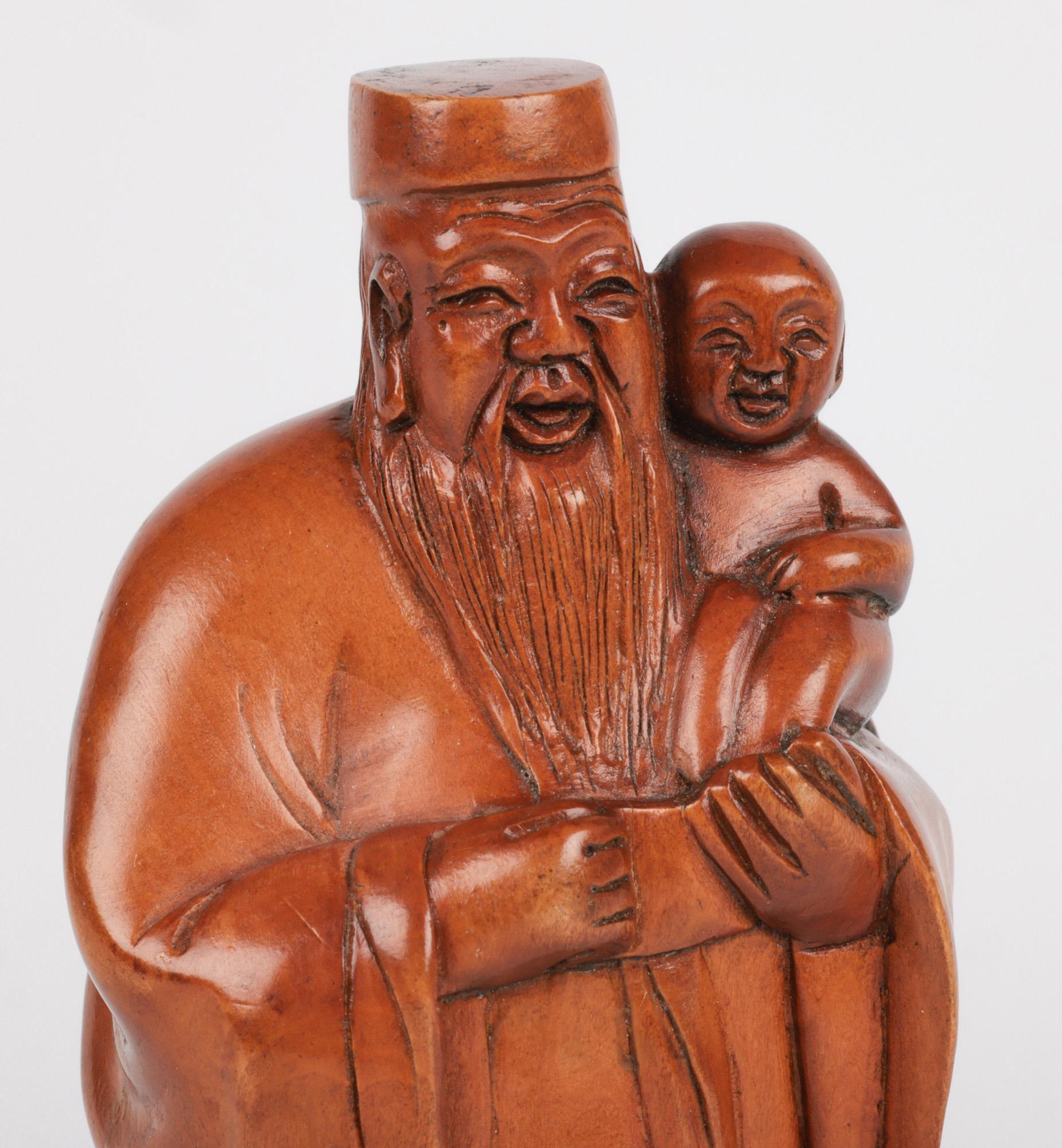 Figure en buis sculptée d'un Immortel tenant un enfant, datant d'environ 1900, de la fin de la période Qing. Le personnage, un homme âgé, est vêtu d'une robe longue et porte un petit chapeau rond et plat. La figure est finement sculptée avec de