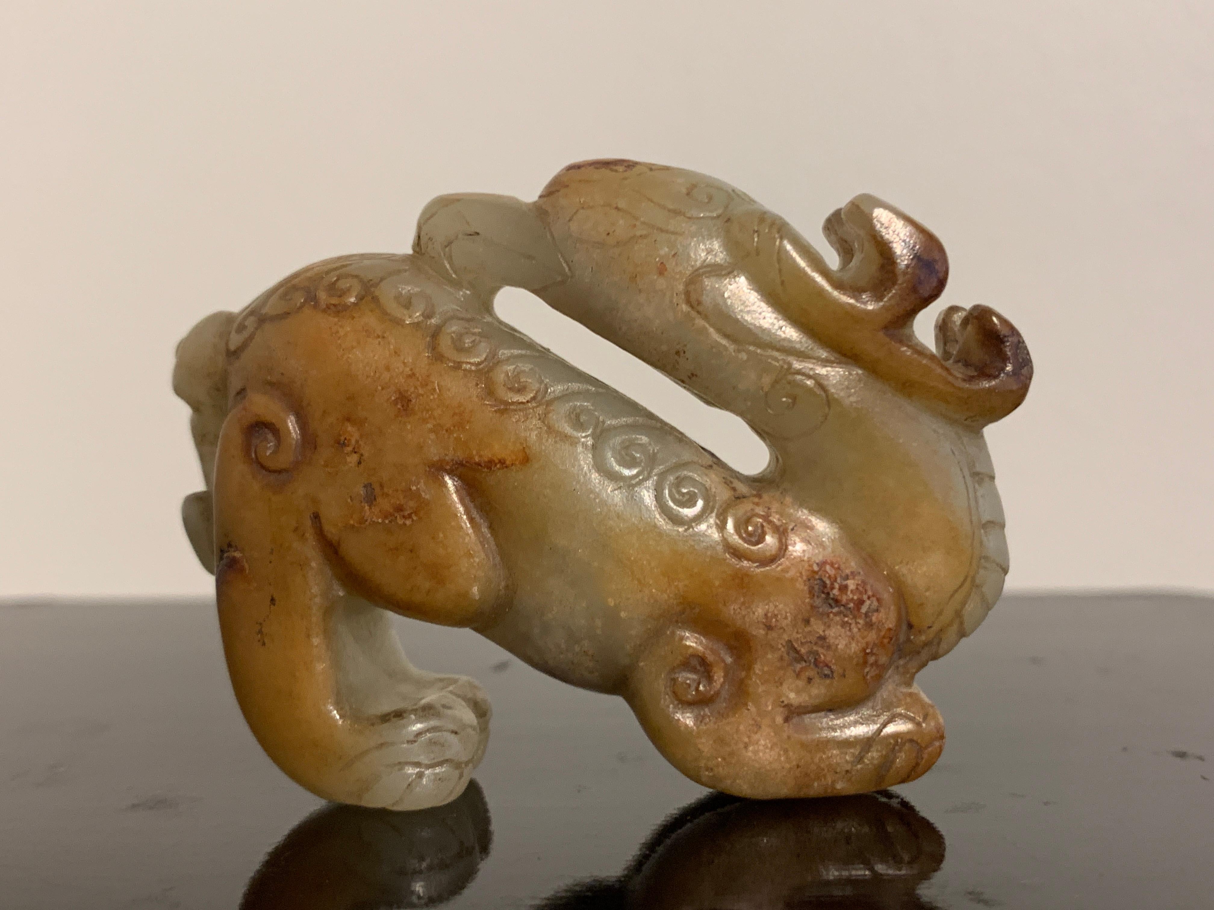 A fine and unusual carving of a mythical animal, possibly a pixiu, of celadon and russet nephrite jade, Ming Dynasty or earlier, China.

The mythical animal masterfully carved as a chimera, with a pair of stag antlers, the head of an eagle, the