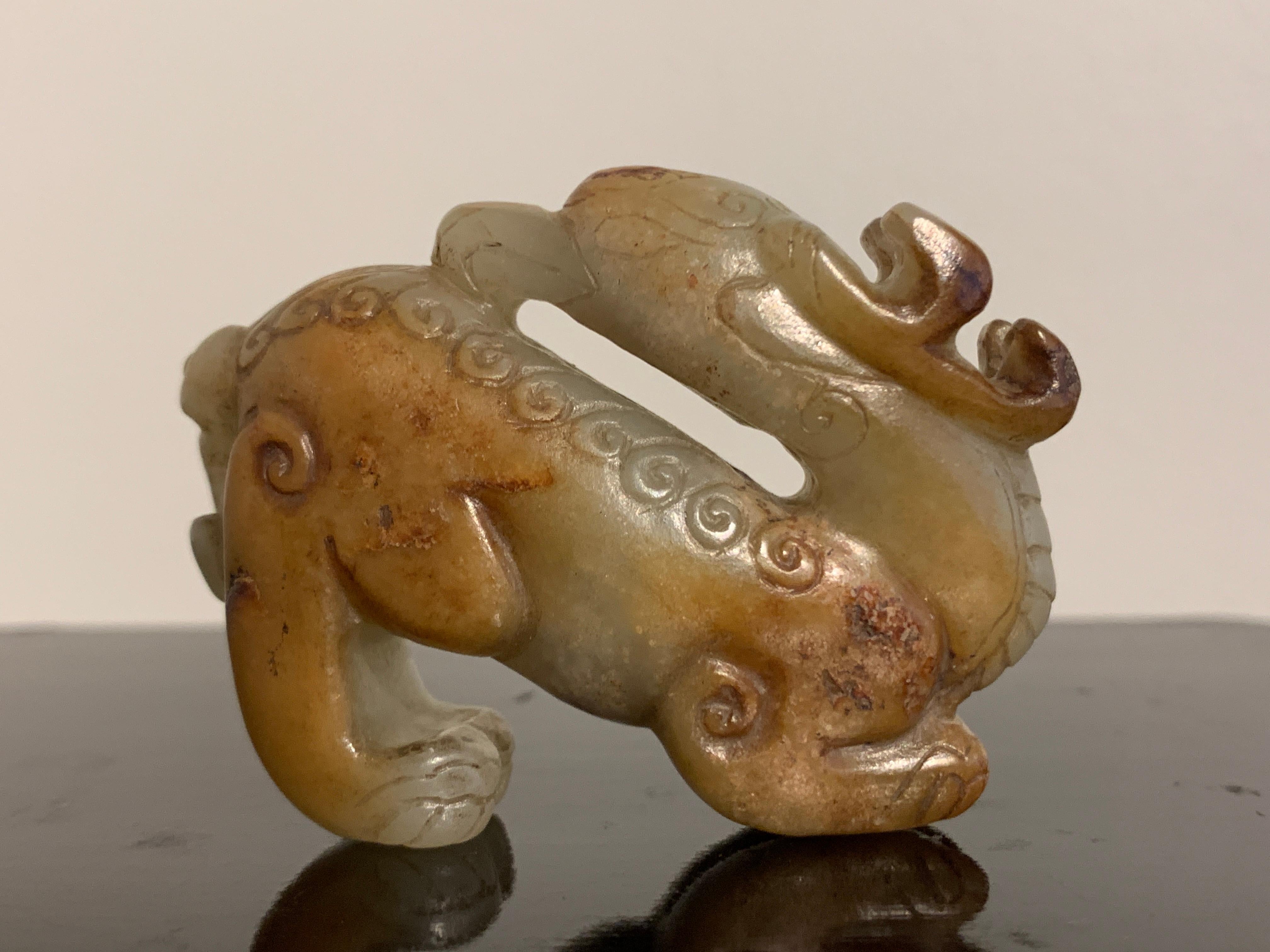Fina e inusual talla de un animal mítico, posiblemente un pixiu, de jade celadón y nefrita rojiza, dinastía Ming o anterior, China.

Animal mítico magistralmente esculpido como una quimera, con un par de astas de ciervo, cabeza de águila, cuerpo