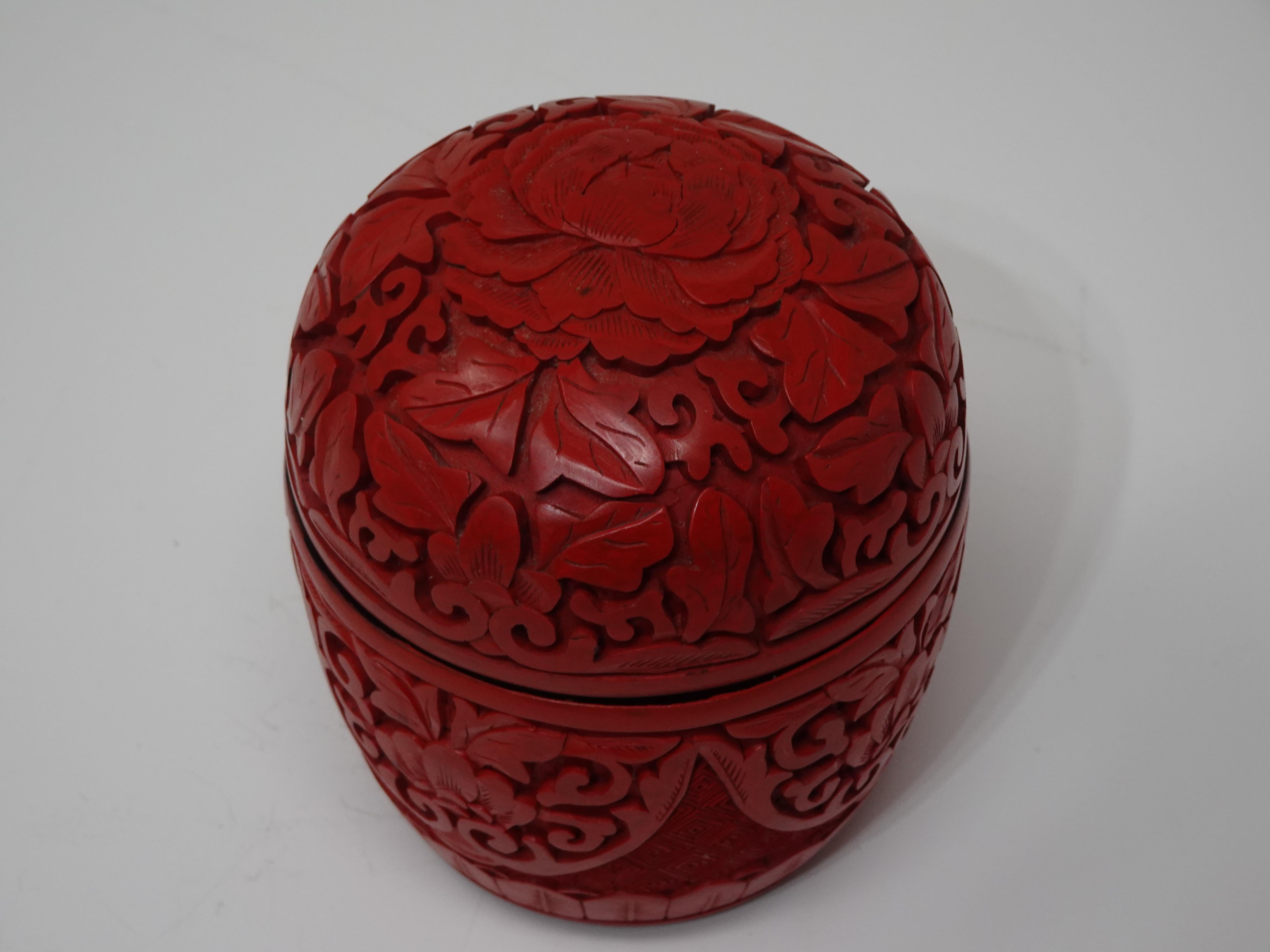 A small Cinnabar lidded container with heavy carving to the top and sides with a flower motif like a Chrysanthemum or lotus. Black coloring to the inside and to the bottom of the piece, a very well crafted and beautifully executed piece of art.