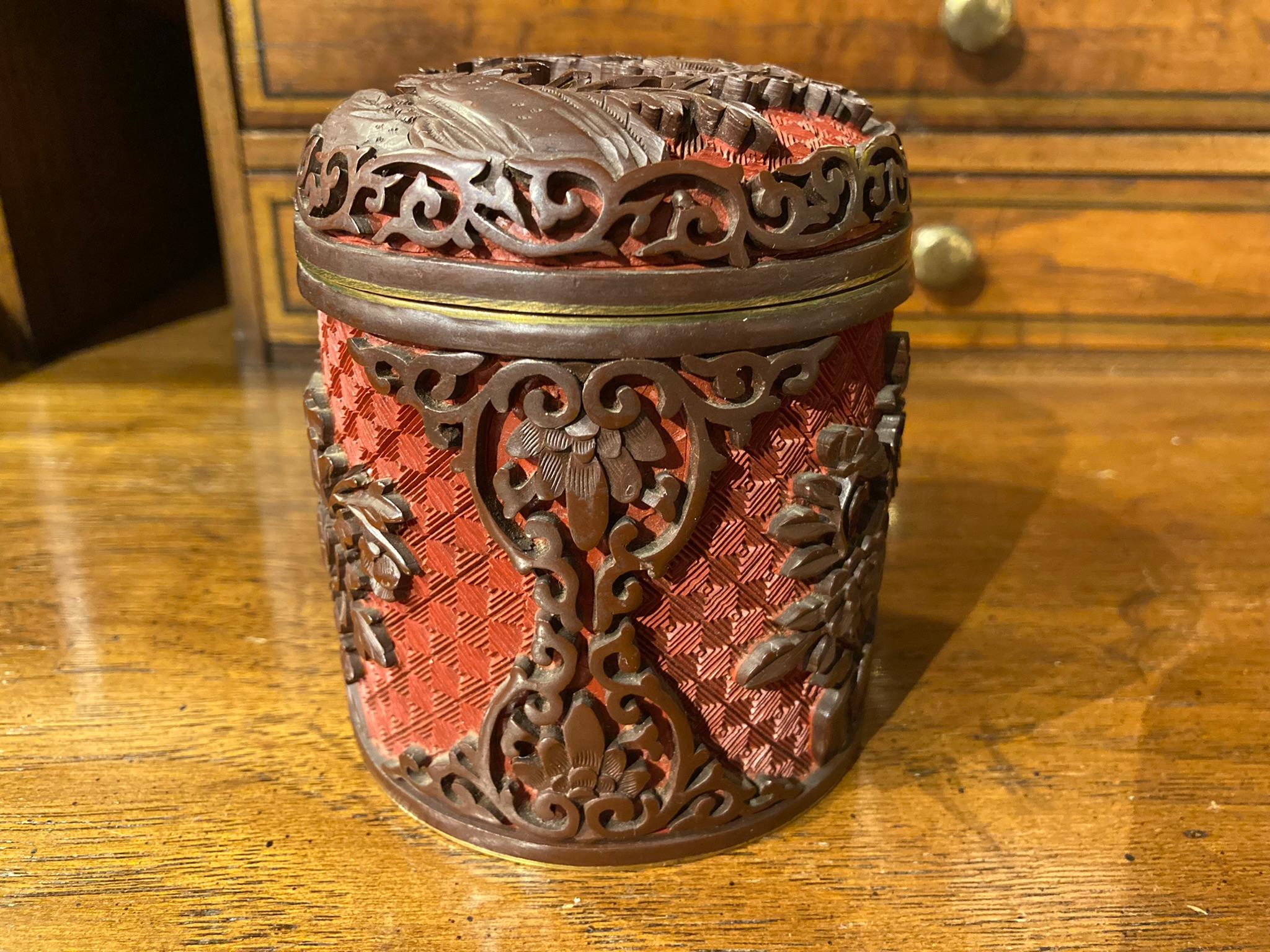 A Chinese covered jar of carved cinnabar covered jar with blue enamel interior over brass. The carving is exquisite, with deep red cinnabar in high relief against a fine background of geometric crosshatching. 
Measures: 3.75 inches high 3.25 wide