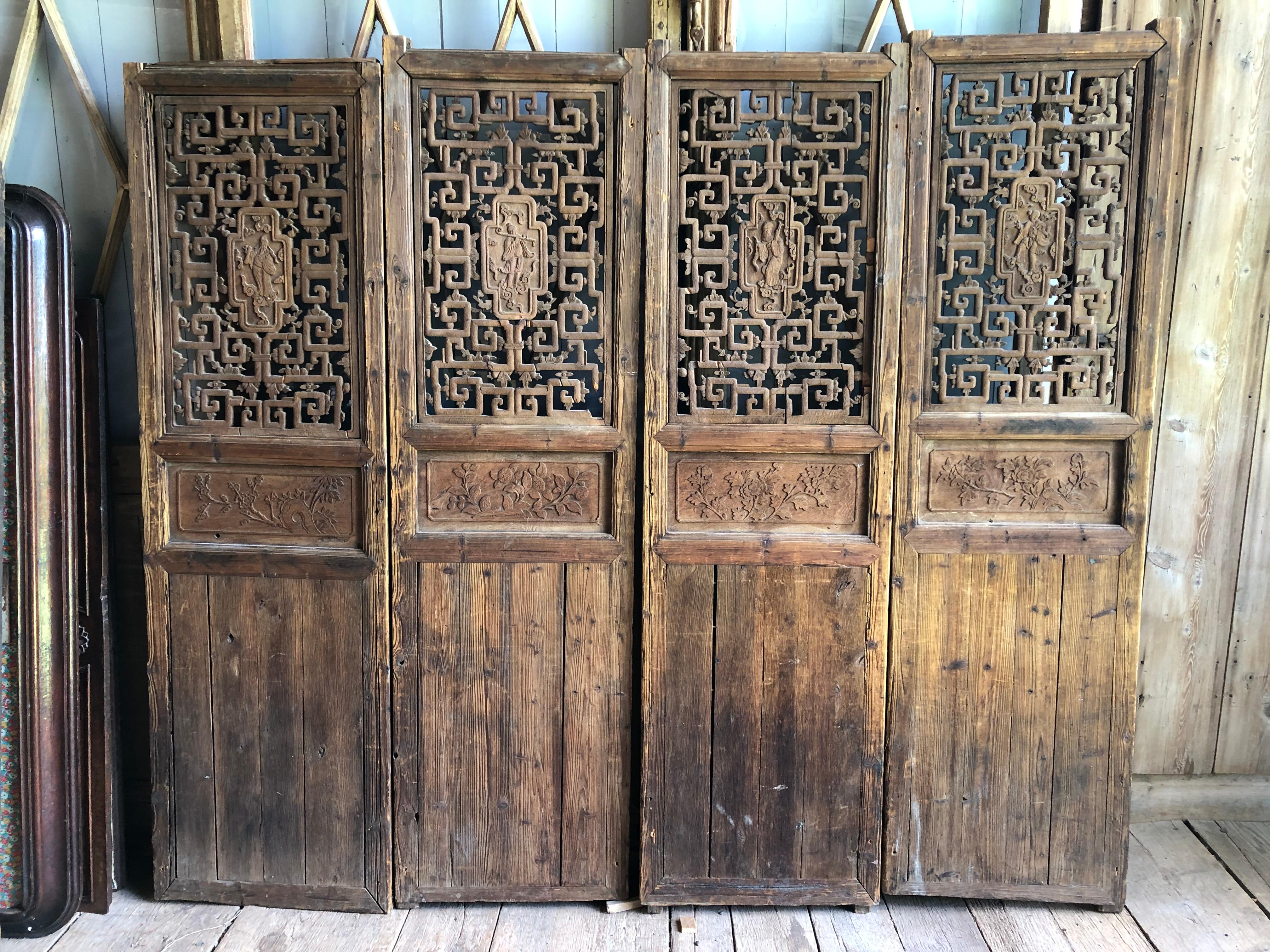 A nice set of 4 carved Chinese doors with pierced decorative panels on the upper half, each with a carved center panel depicting male and female figures. The doors are in pine or cedar and have solid panels on the back that slide up to cover the