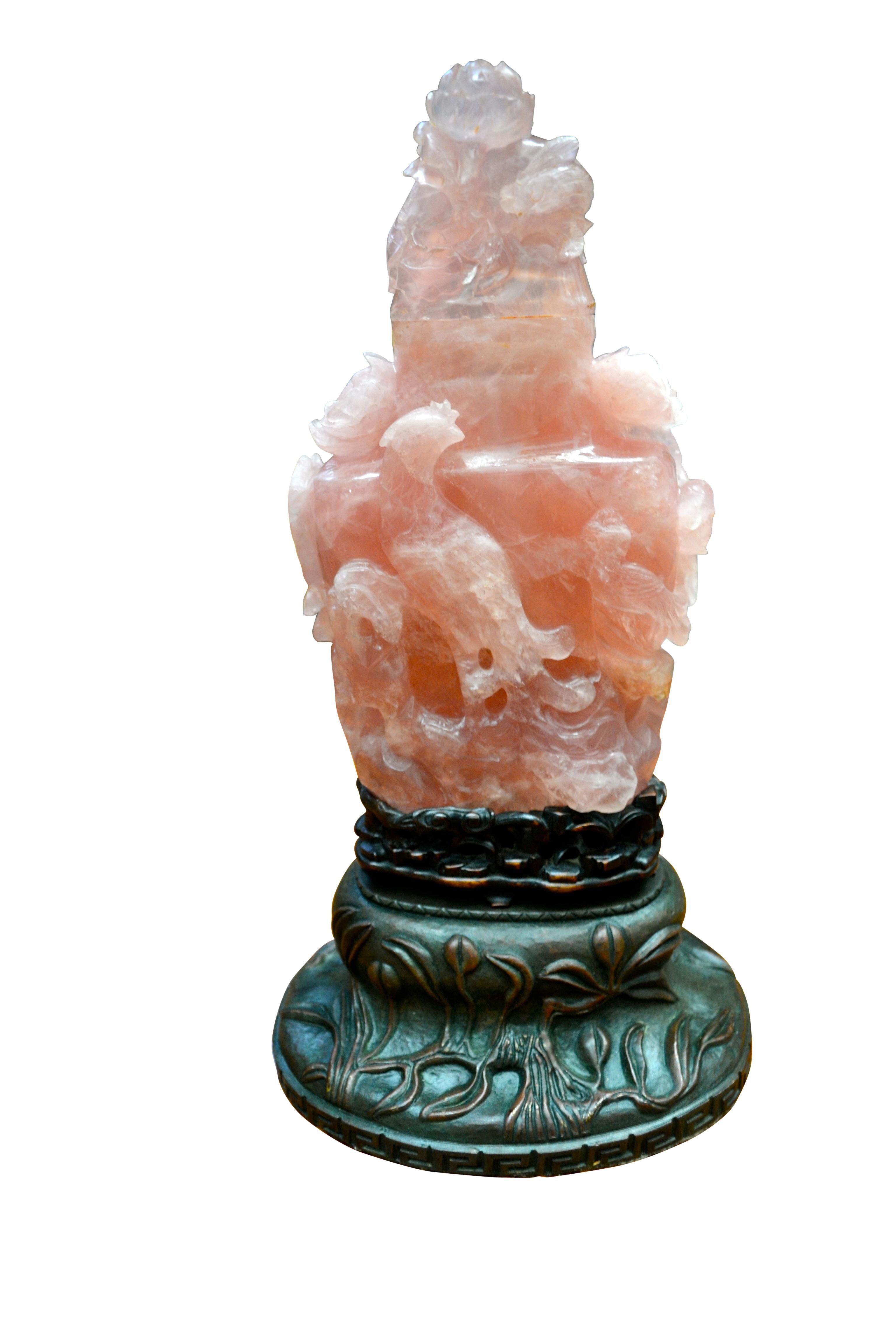 A decorative Chinese carved pink fluorite lamp of vase shape. The stone is carved in the round with exotic birds, peonies and the detachable top is carved as a stylized carp. The 'vase' sits on a carved polished wood base on a further decorated