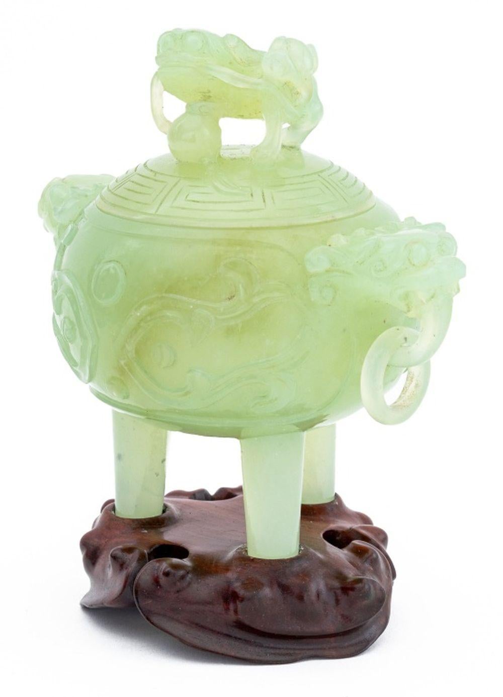 Chinese Carved Jade Foo Dog Covered Tripod Censer, with incised taotie design to each side and two dragon head mask handles with ring, surmounted by foo lion, on fitted carved wood stand. Overall: 5.75
