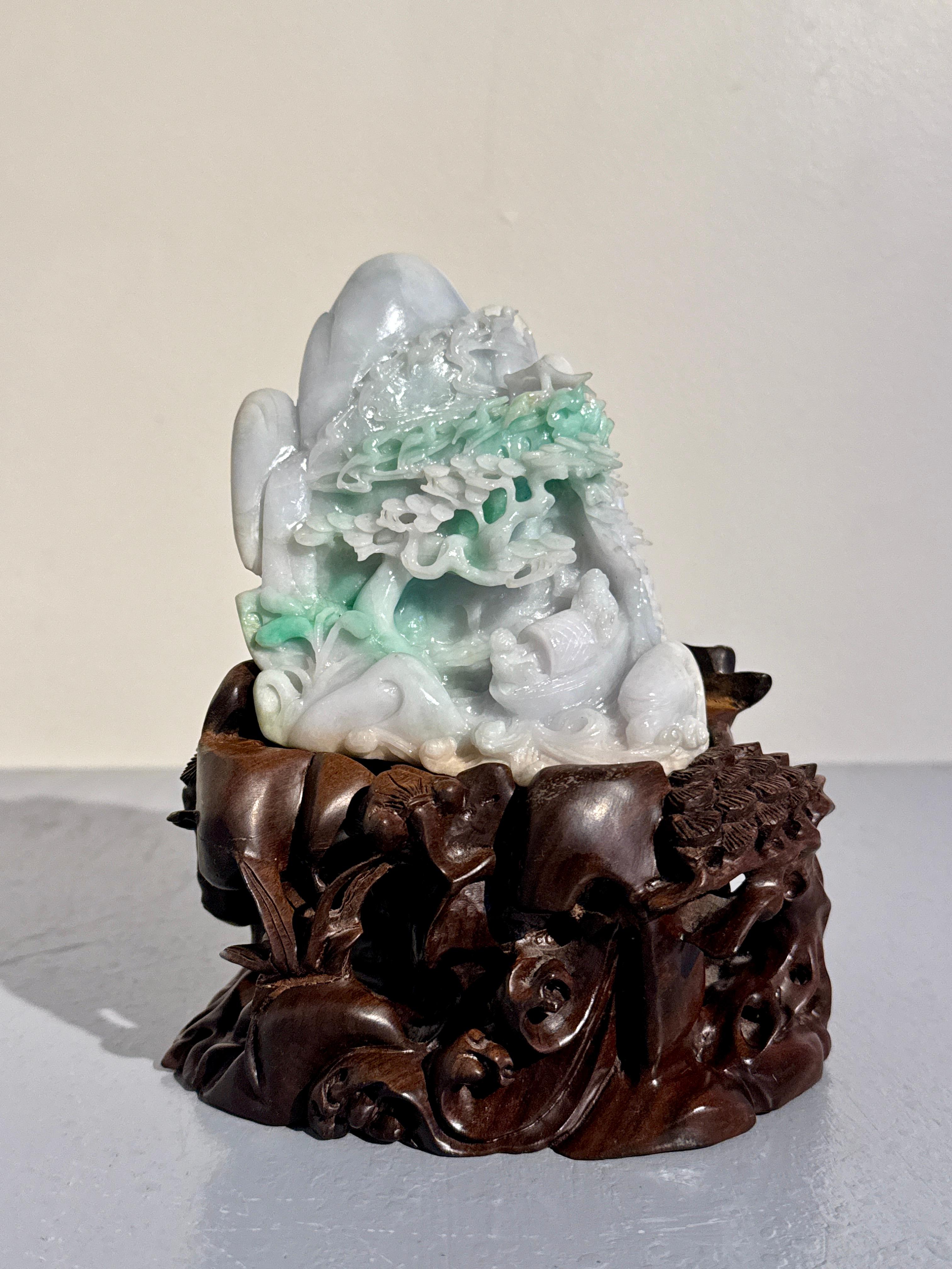 Bloc de jadéite (fei cui) vert et blanc grisâtre finement sculpté, avec une scène de montagne et de grotte, présenté sur un support en bois dur nanmu sculpté, milieu ou fin du 20e siècle, Chine.

Le bloc est composé d'un seul spécimen grand et dense