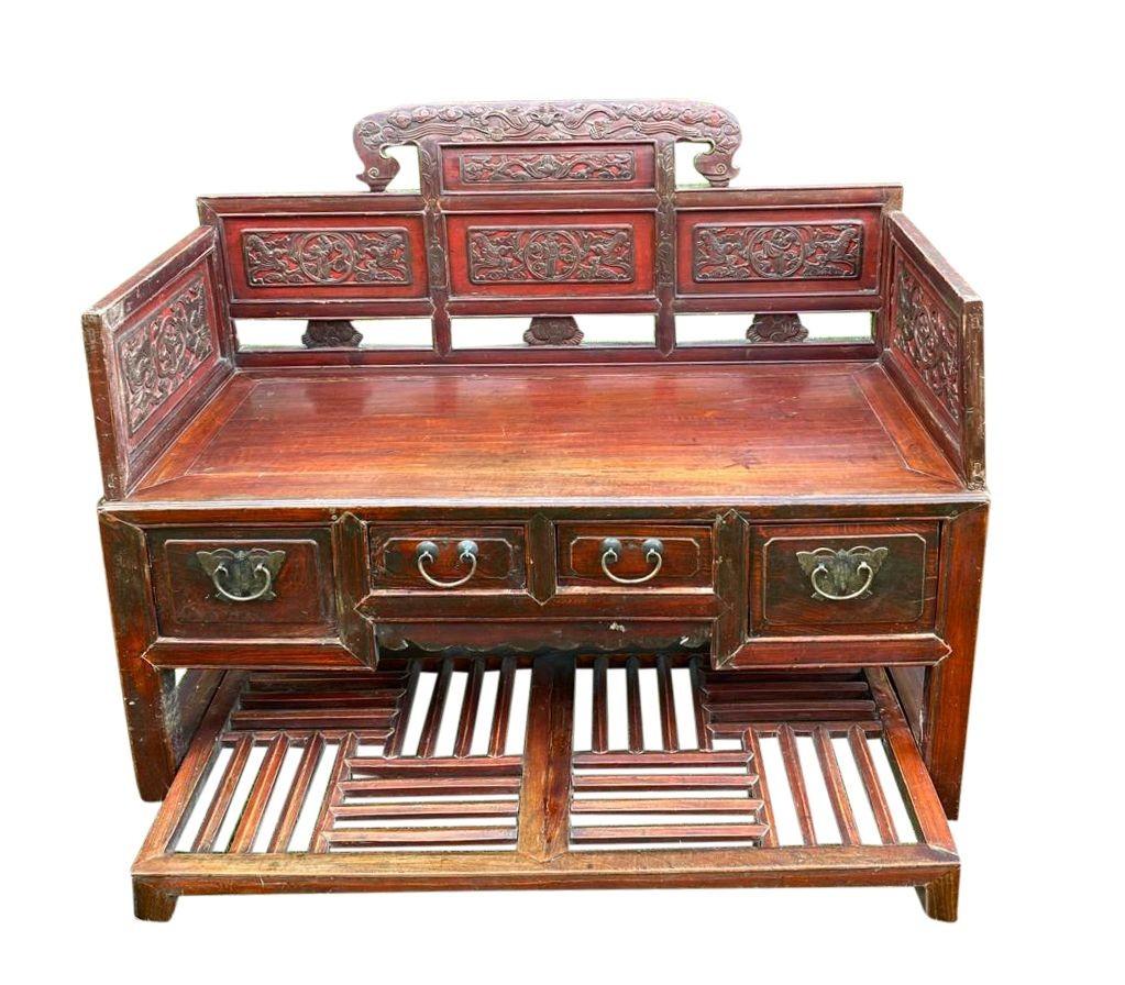 A very decorative late 19th century Chinese sofa with hand carved decoration to the back rest, a slated foot rest and drawers beneath the seat. Having a red stained and lacquer patina.