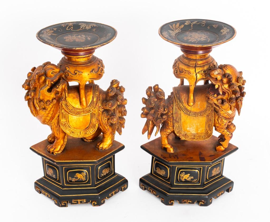 Pair of Chinese hand-carved wood candle stands, one in the form of a qilin and one a foo lion, both atop hexagonal ebonized pedestals and balancing tripod censers atop their backs, with hand-painted gilt floral accents.

Dimensions: Each: 11