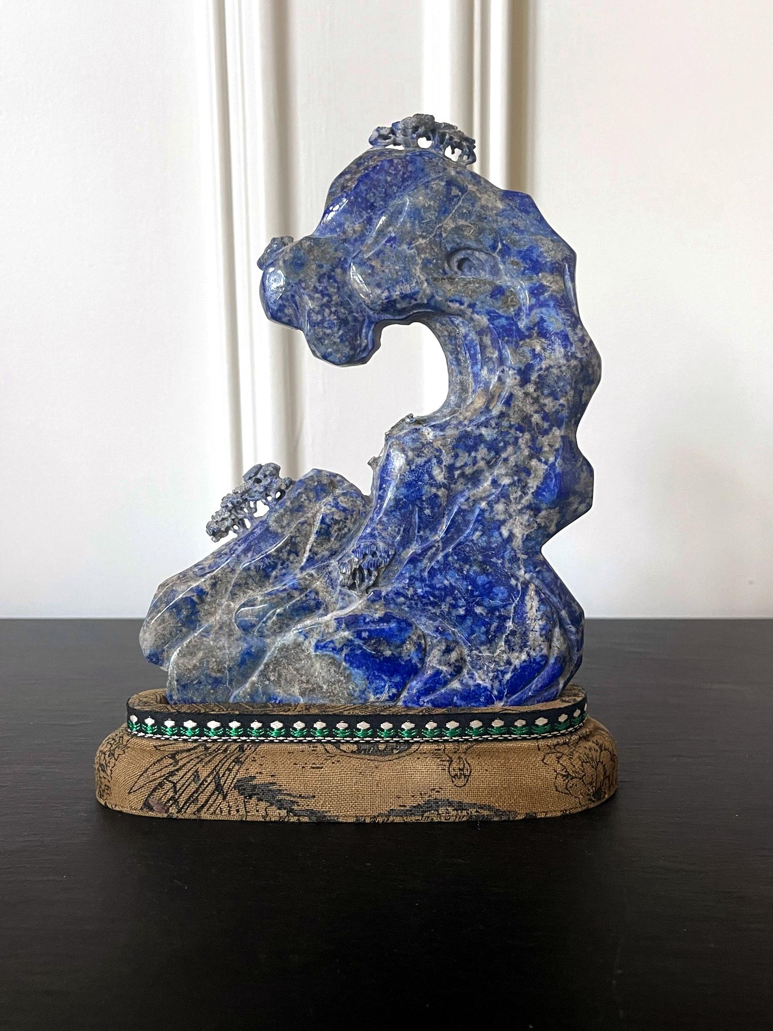 A Chinese scholar rock carved from a natural lapis stone and displayed on a brocade wrapped stand circa late 19th century Qing Dynasty. The brightly blue lapis was considered as am exotic gemstone in China and mostly imported from Persia through the