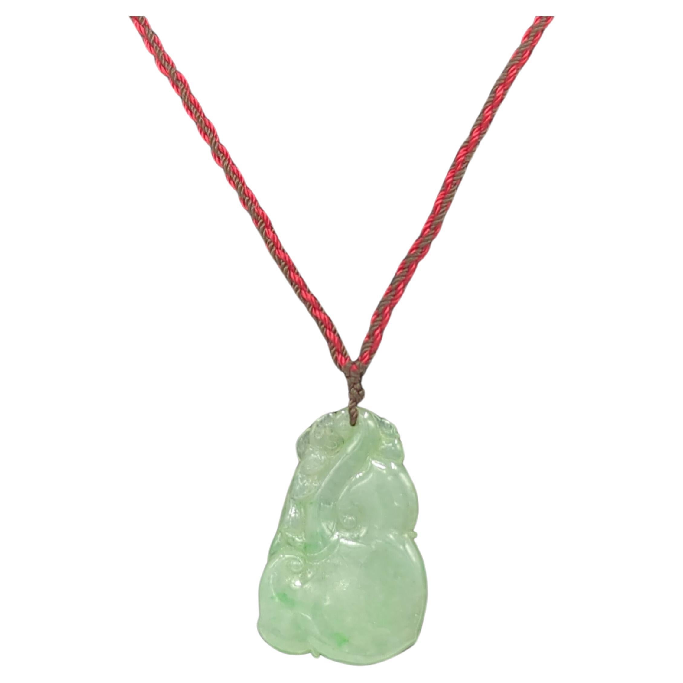 A finely carved and polished translucent jadeite pendant, light green with spot green inclusions, in the form of a stylized ruyi, on a pull string cord necklace with overall length adjustable from 18-24
