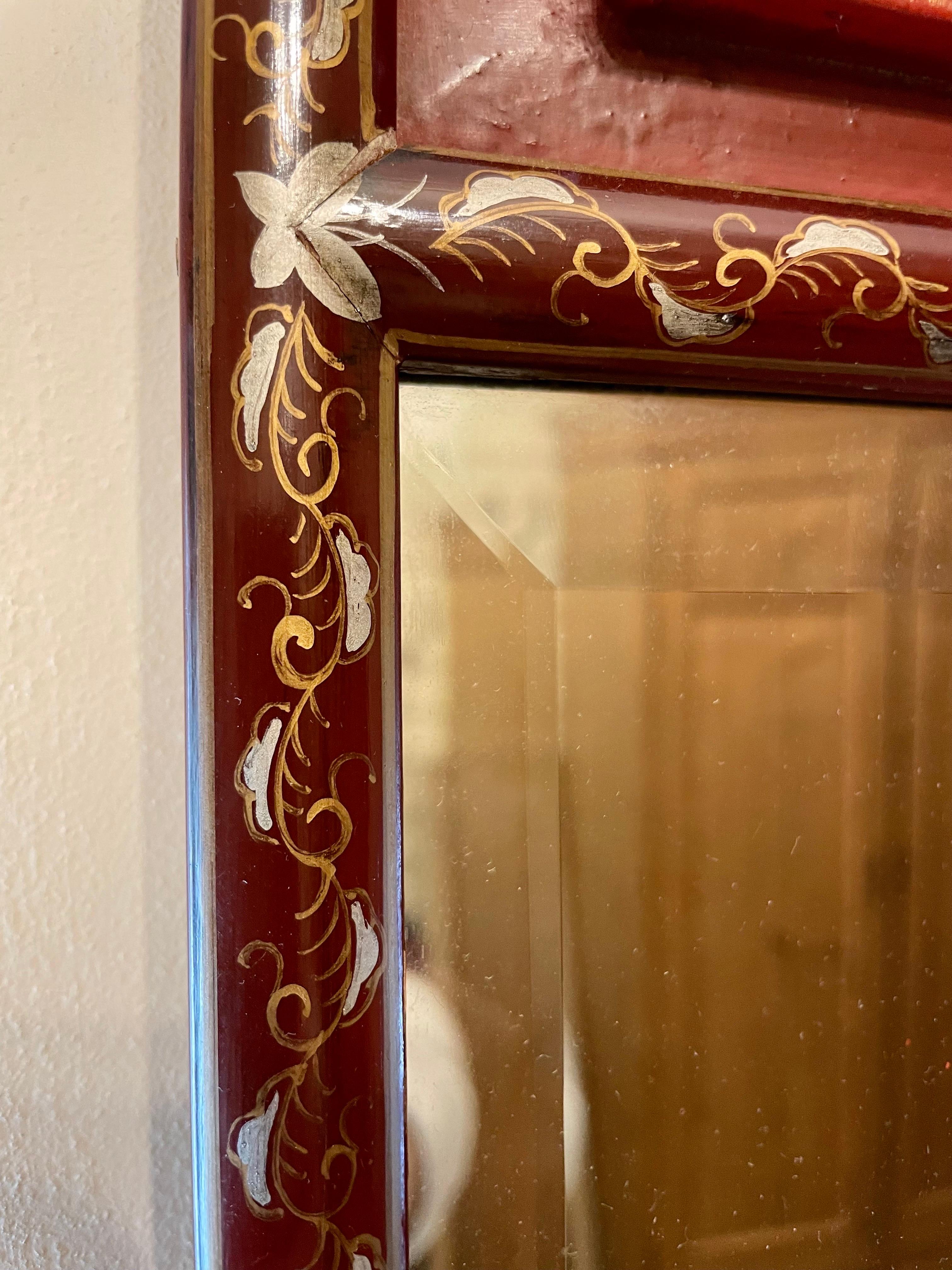Chinese Carved Gilt  Beveled Mirror with painted details around oxblood colored lacquered wood frame. Carve panel at top is gold gilt finished. Brass detail at top. Wire on back for hanging. Very nice decorative mirror, good overall condition, with