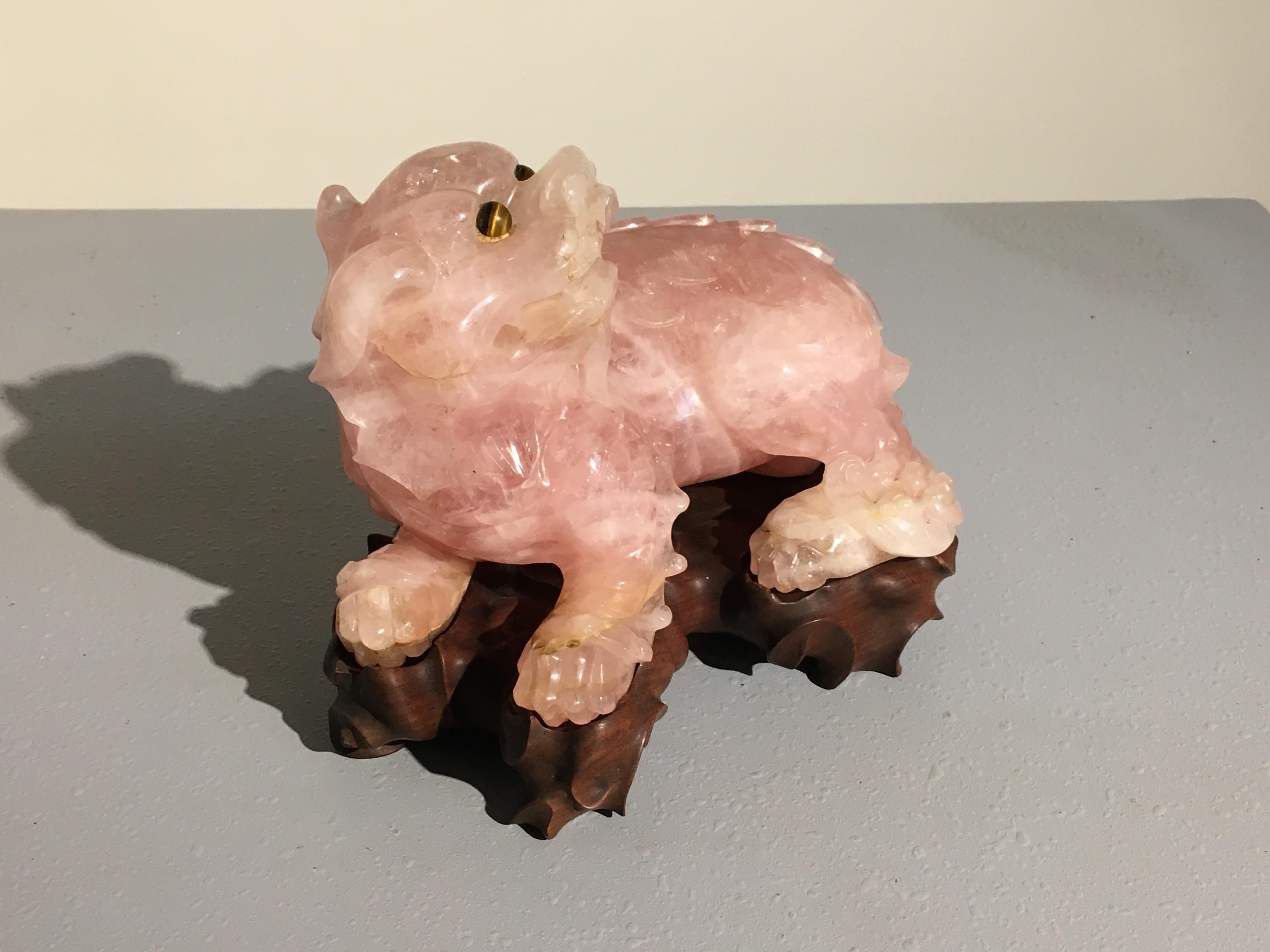 Chinese Republic Period carved rose quartz foo lion with tiger eye eyes, circa 1930s, China.

The foo lion, also known as a foo dog, is well carved from a single large piece of mottled pink rose quartz. The lion portrayed hunched down in a playful