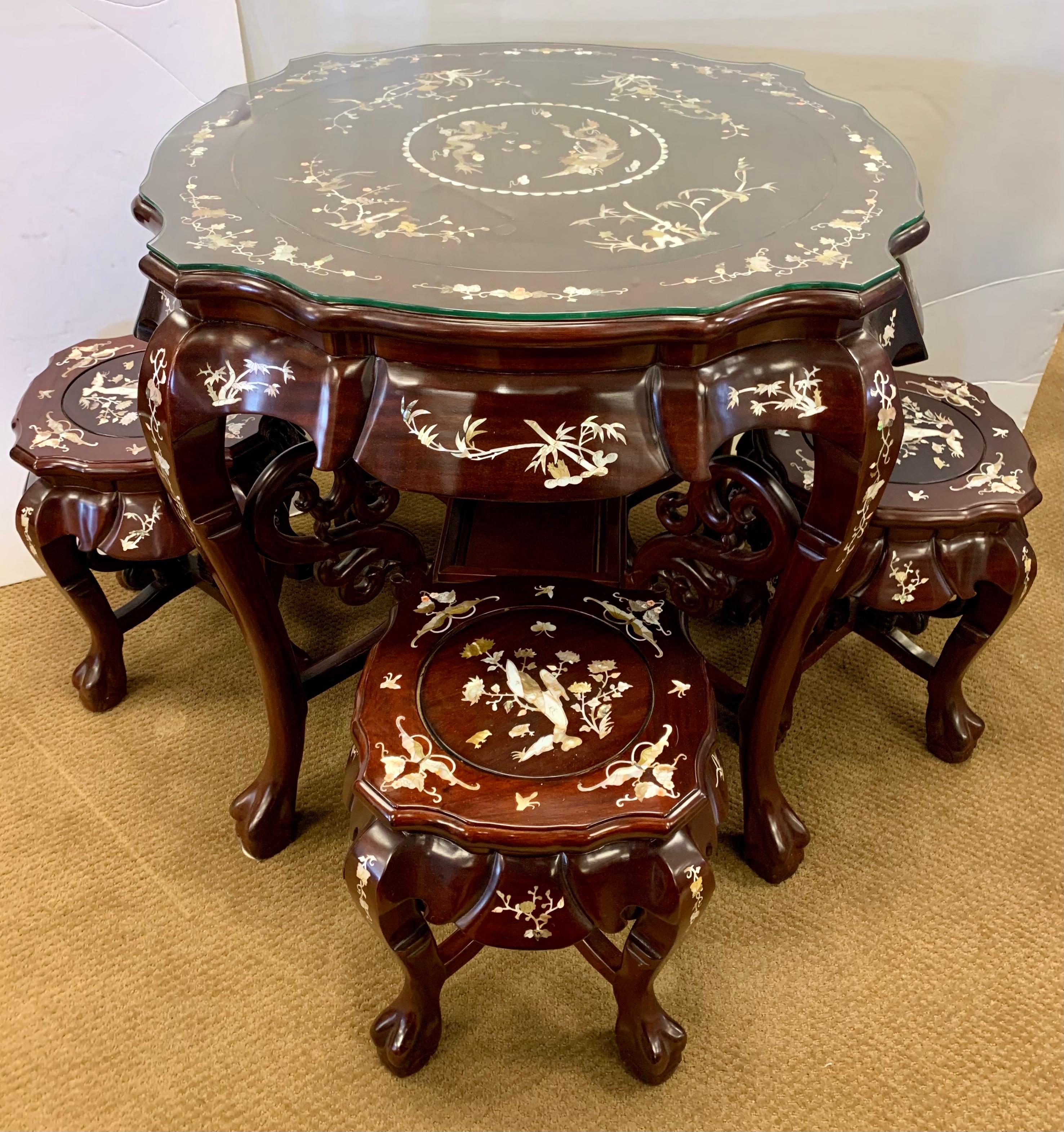 Intricately carved Chinese inlaid mother-of-pearl tea table, crafted from high quality rosewood. Inlay continues throughout the legs and frame, with four stools inlaid with floral motifs and a center scene of birds and butterflies. Tables and stools