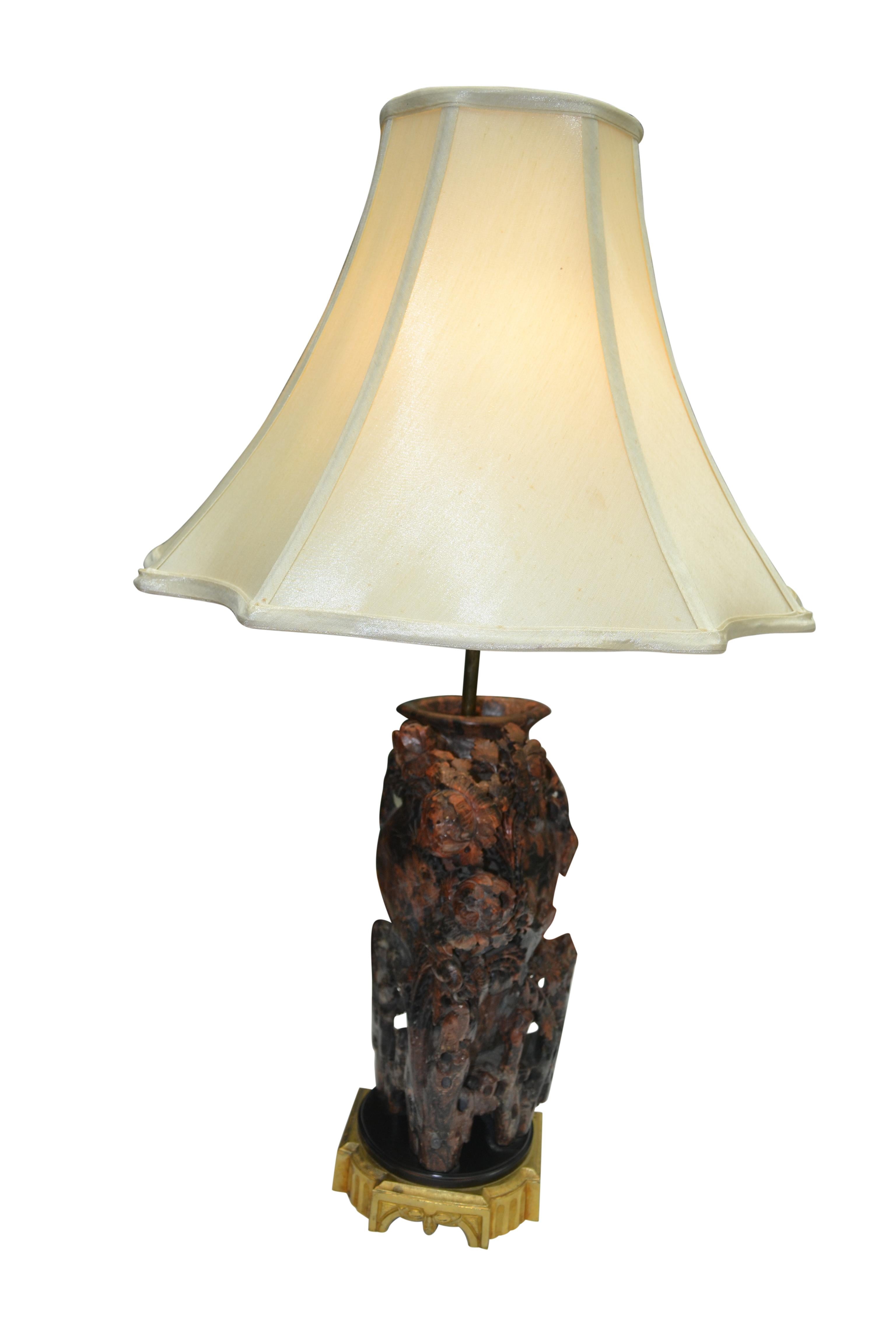 A carved soapstone lamp base, unusual because of the color of the stone; reddish, brown and black. The carving is in the shape of a vase which is almost totally encrusted in 'branches' and flowers and buds. There is a great deal of all-over open