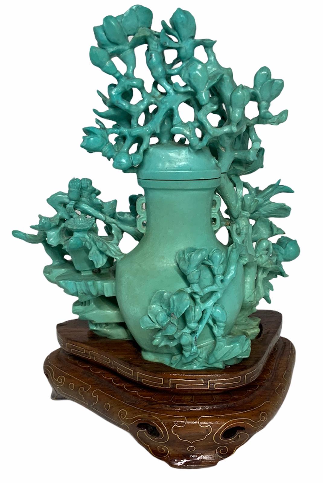 Mix of flowers arrange like a bonsai tree hiding a vase in the back. The scene is completed with two kittens, one that is playing with the branches and the other is observing it. The carving is this most likely Persian turquoise stone stands over a